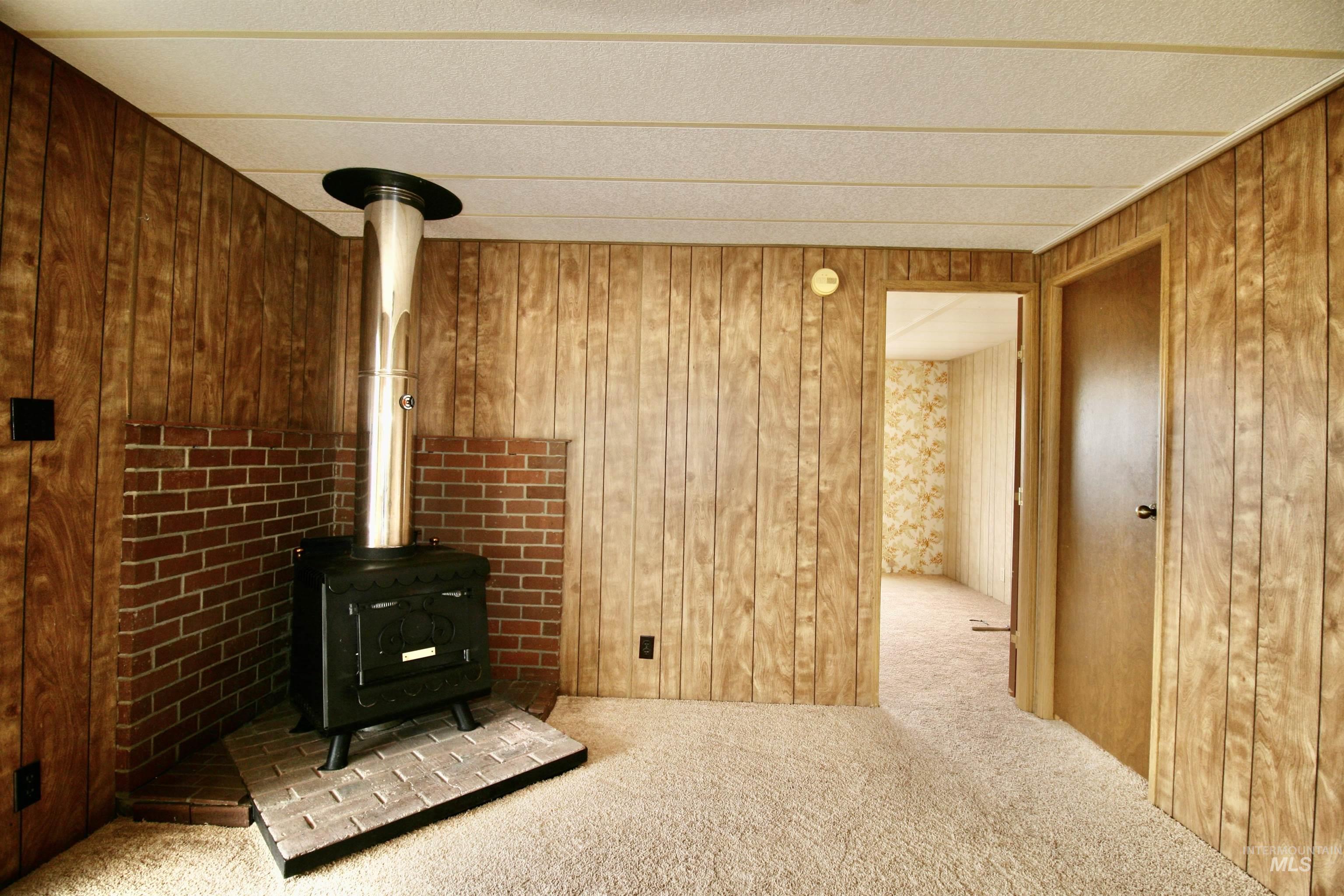 Unfurnished living room with a wood stove, carpet flooring, and wood walls