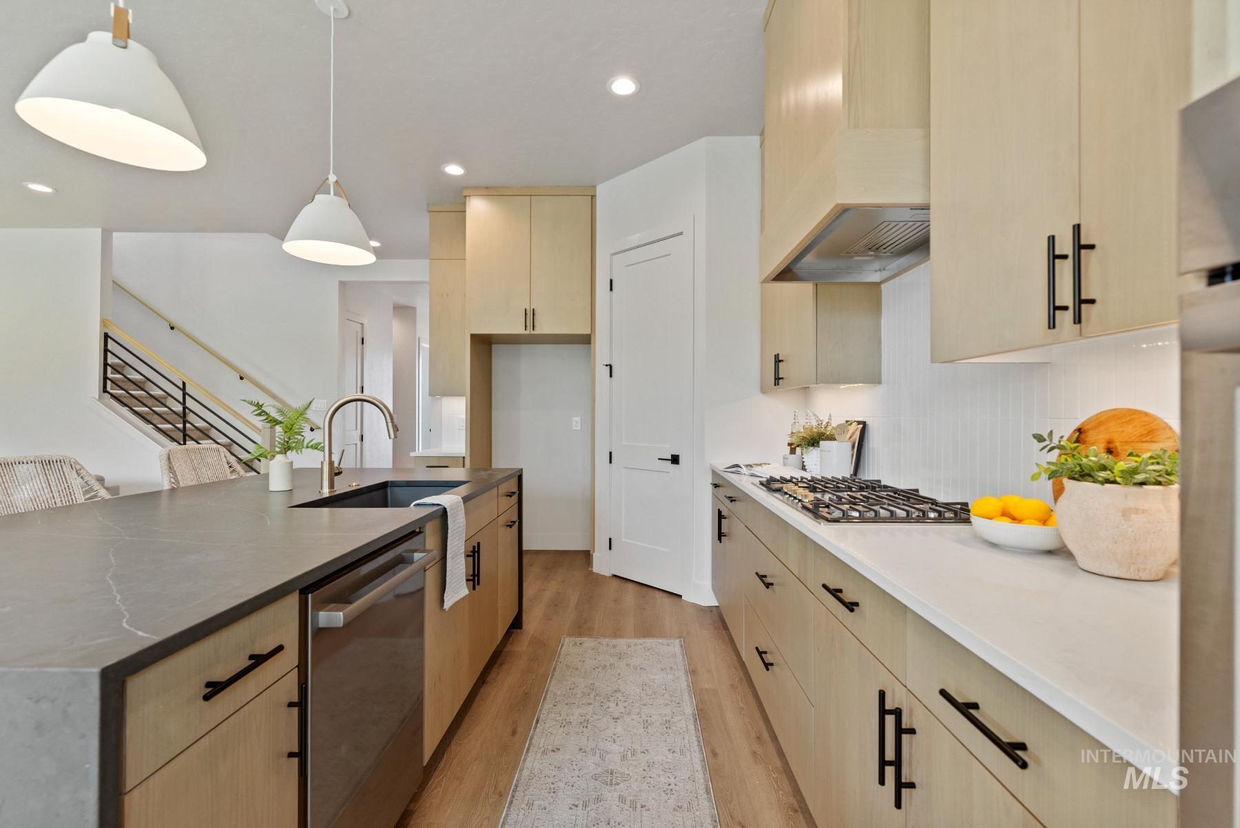 Kitchen featuring light wood finished floors, light brown cabinetry, stainless steel appliances, recessed lighting, and hanging light fixtures