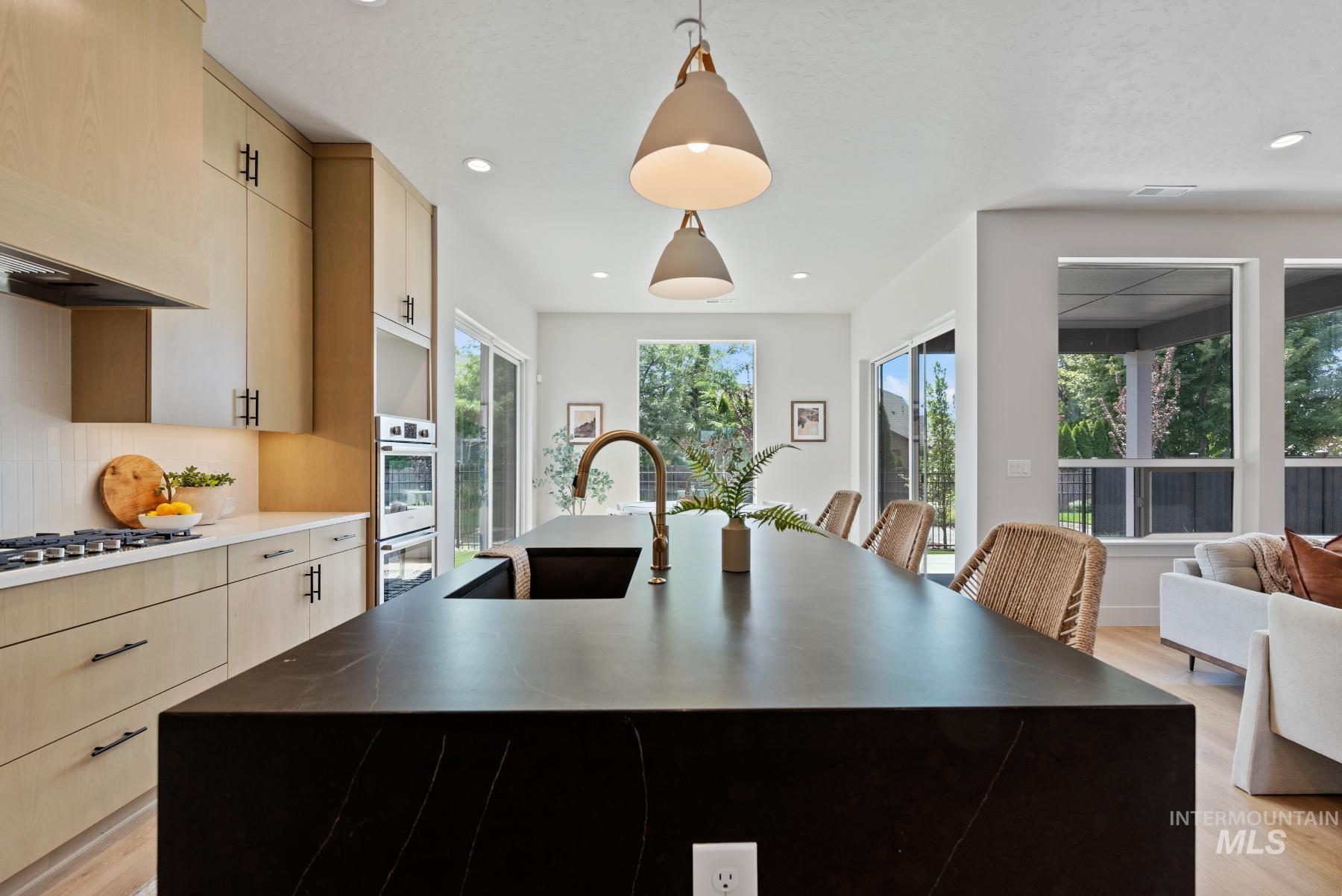Kitchen featuring light wood-style flooring, light brown cabinetry, decorative light fixtures, a center island with sink, and tasteful backsplash
