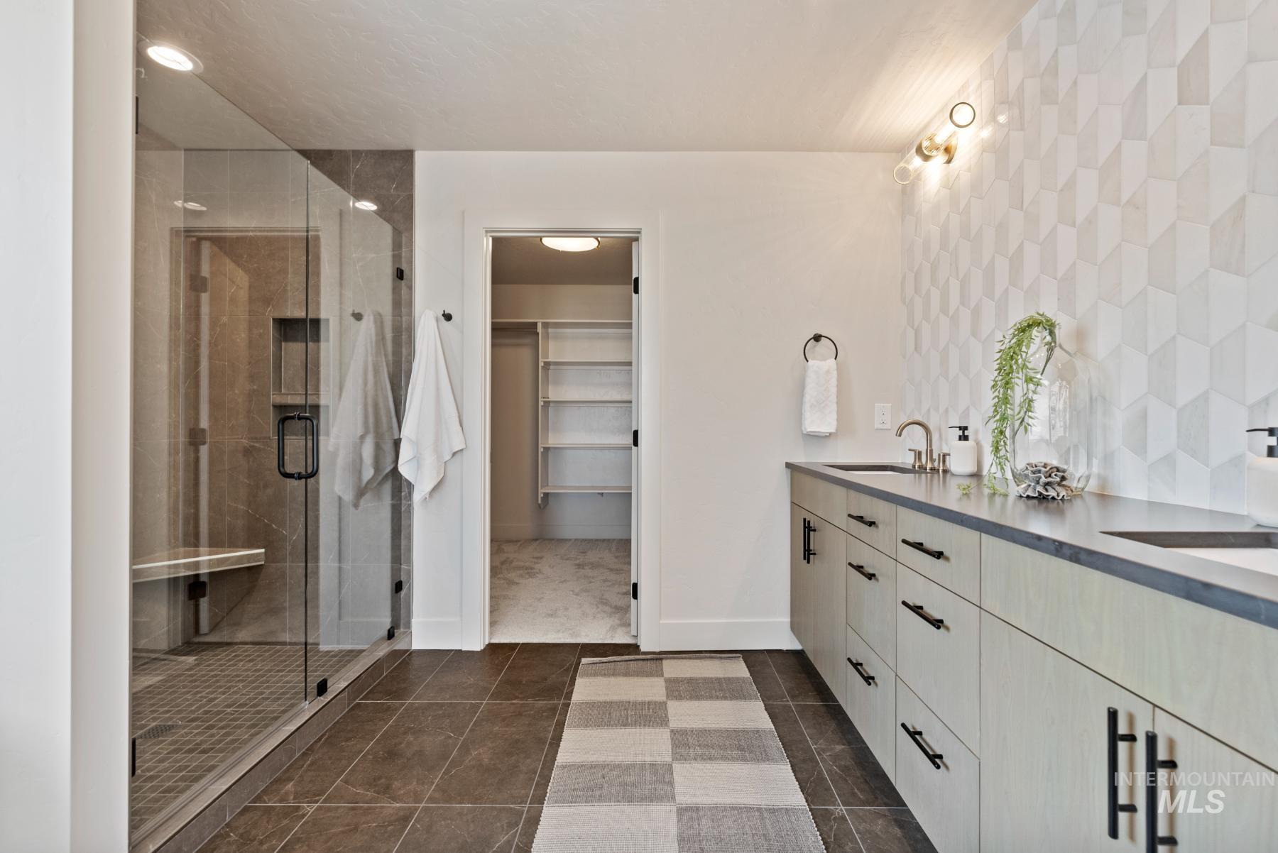 Bathroom featuring a walk in closet, double vanity, a shower stall, dark tile patterned flooring, and backsplash