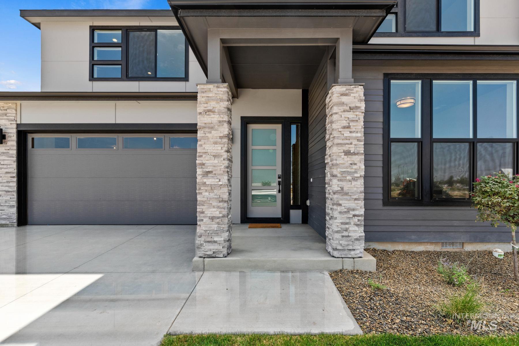 Property entrance featuring an attached garage, driveway, stone siding, and stucco siding