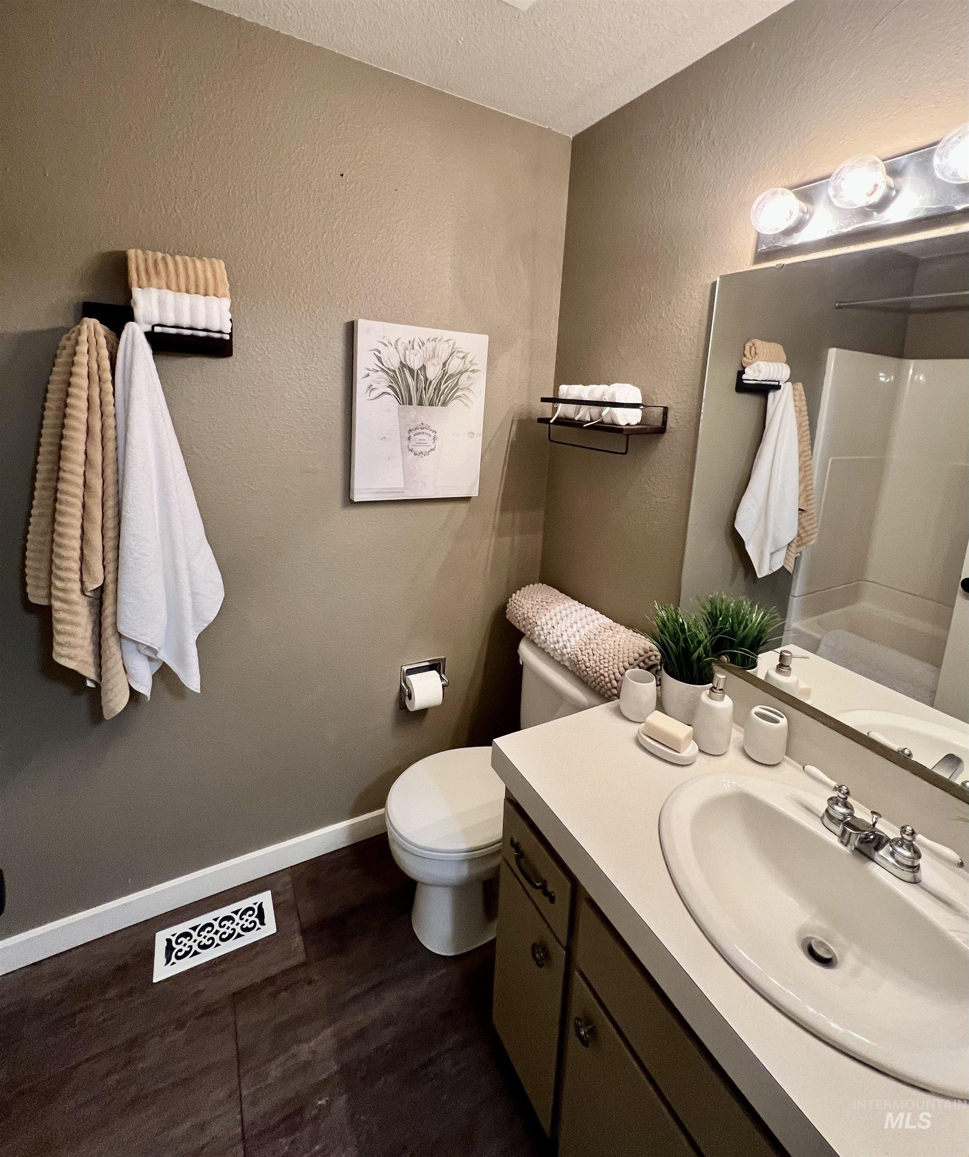 Full bathroom featuring a textured wall, vanity, a textured ceiling, a shower, and dark wood-style floors