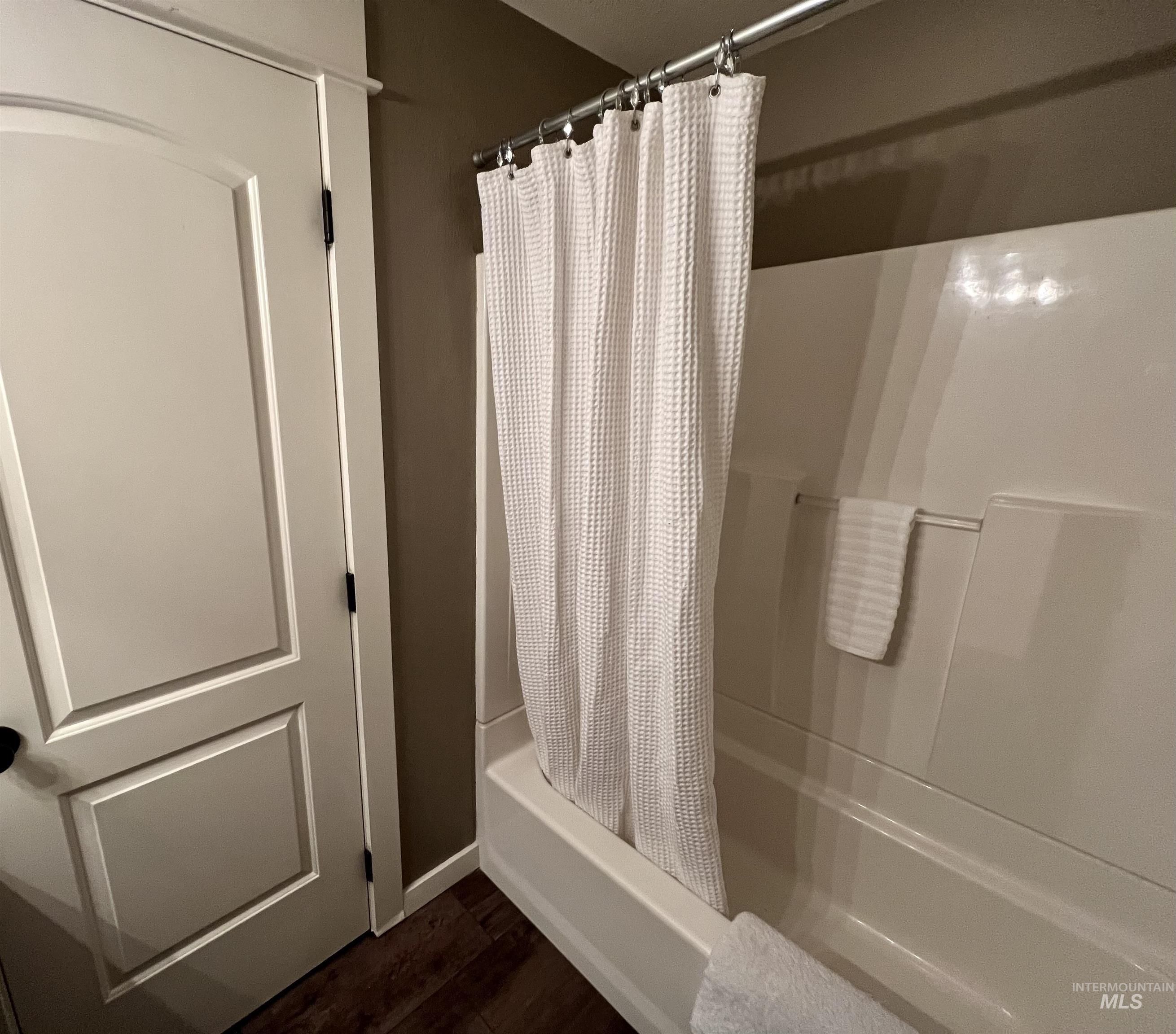Bathroom with shower / tub combo and dark wood-type flooring