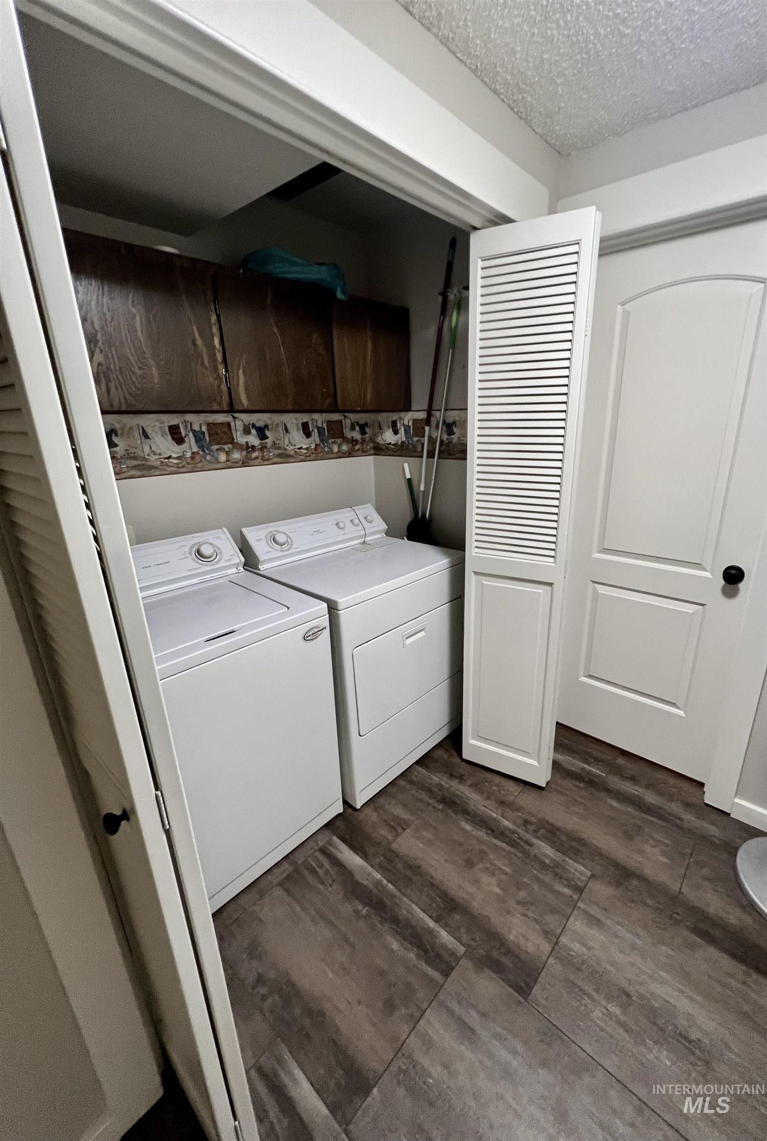 Laundry area with a textured ceiling, dark wood-style floors, washing machine and clothes dryer, and cabinet space