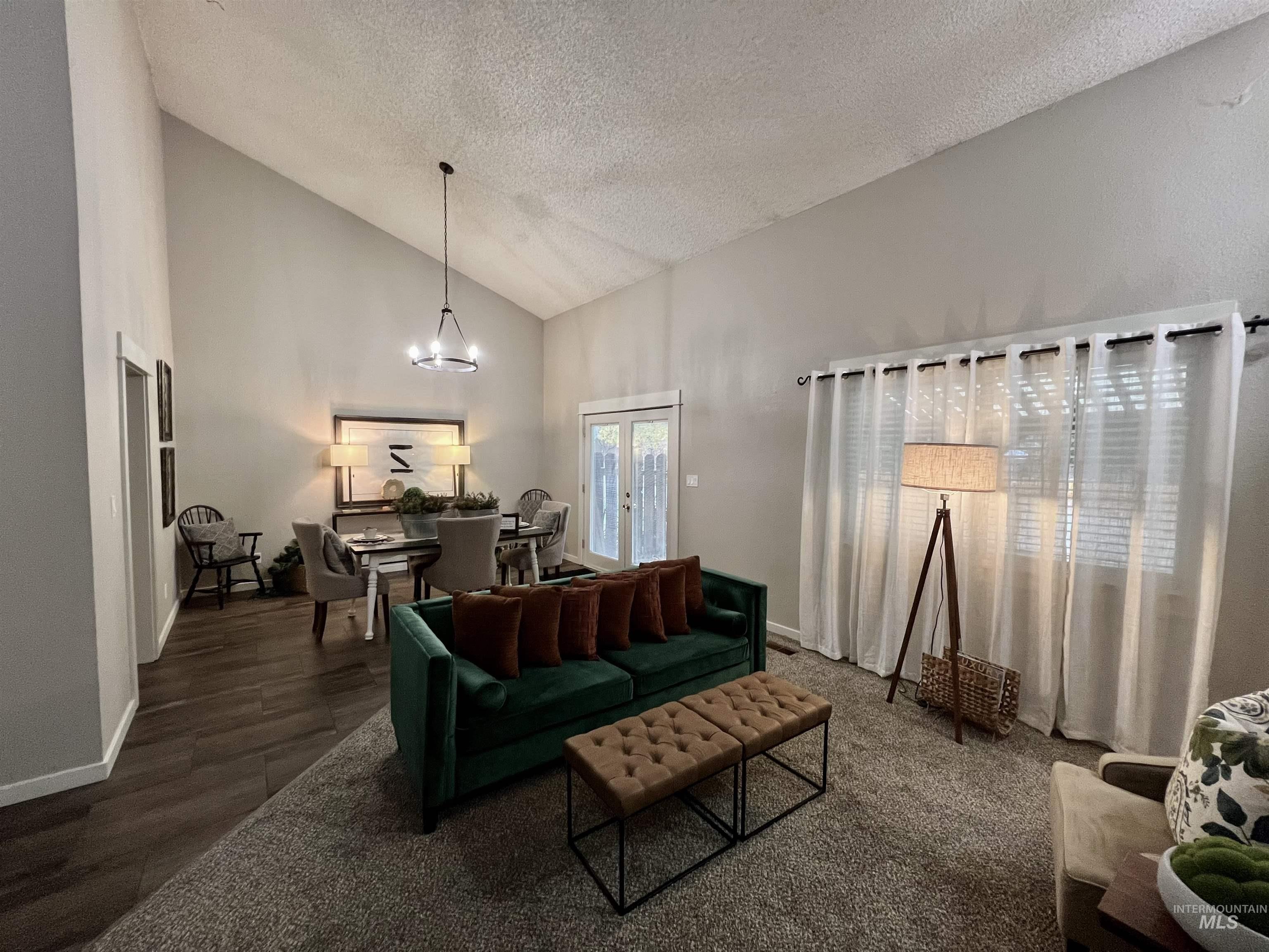 Living room with high vaulted ceiling, a textured ceiling, a chandelier, and wood finished floors