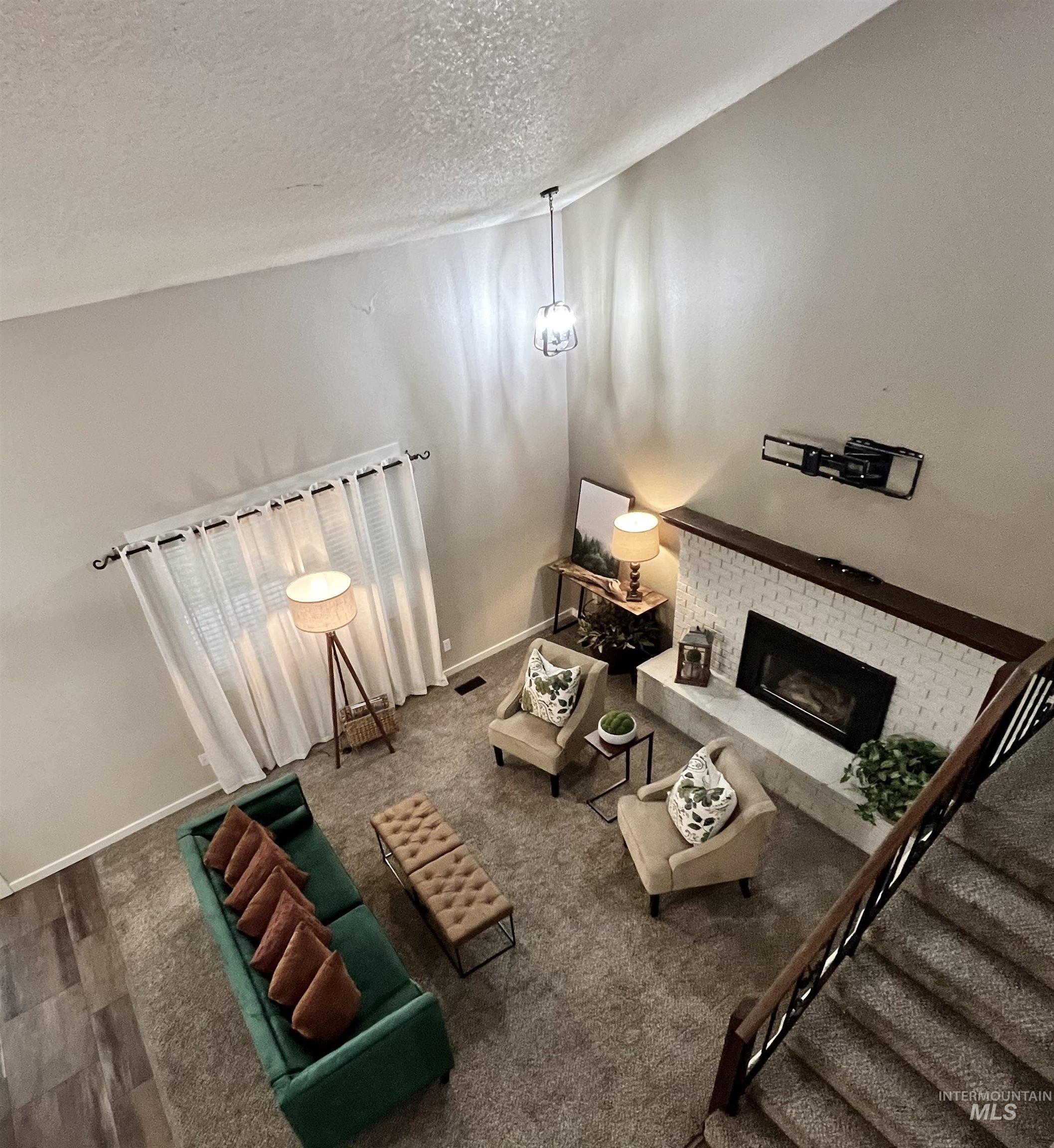 Carpeted living area featuring a fireplace, a textured ceiling, and stairway