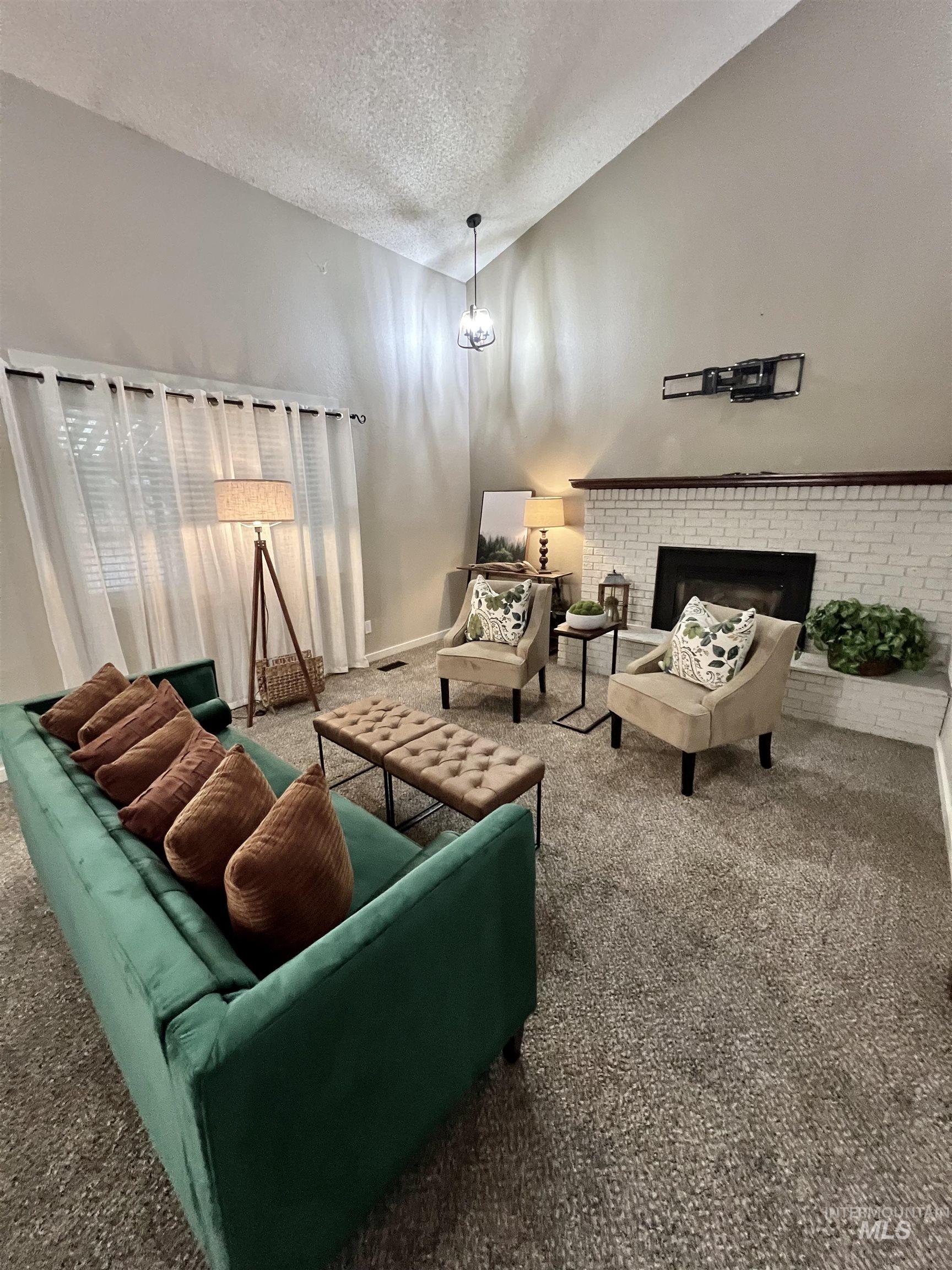 Carpeted living room featuring a fireplace, a textured ceiling, and lofted ceiling