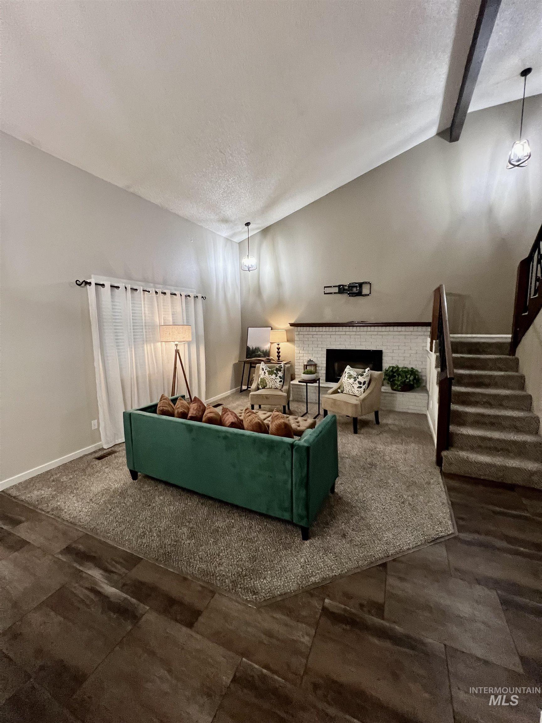 Living area featuring a textured ceiling, stairway, vaulted ceiling, a chandelier, and a brick fireplace