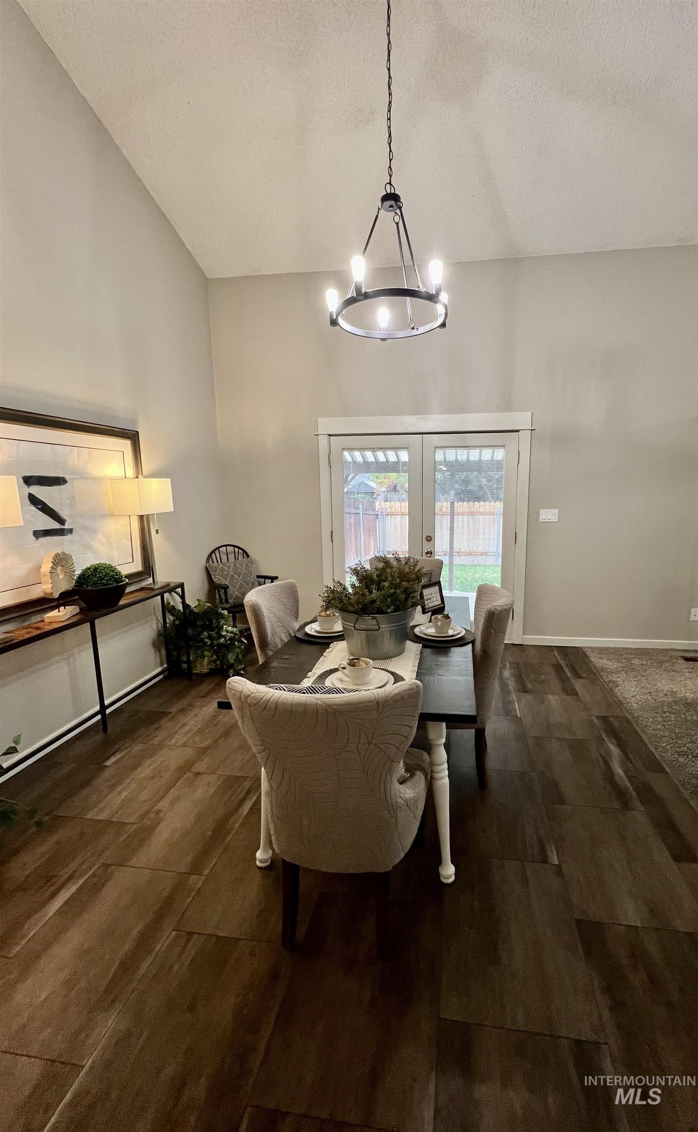 Dining area featuring french doors, a textured ceiling, dark wood-style floors, a chandelier, and vaulted ceiling