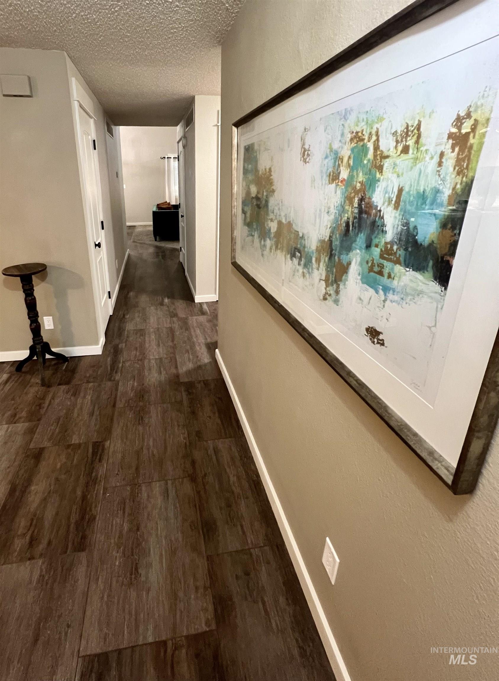 Hallway with dark wood-type flooring, a textured ceiling, and a textured wall