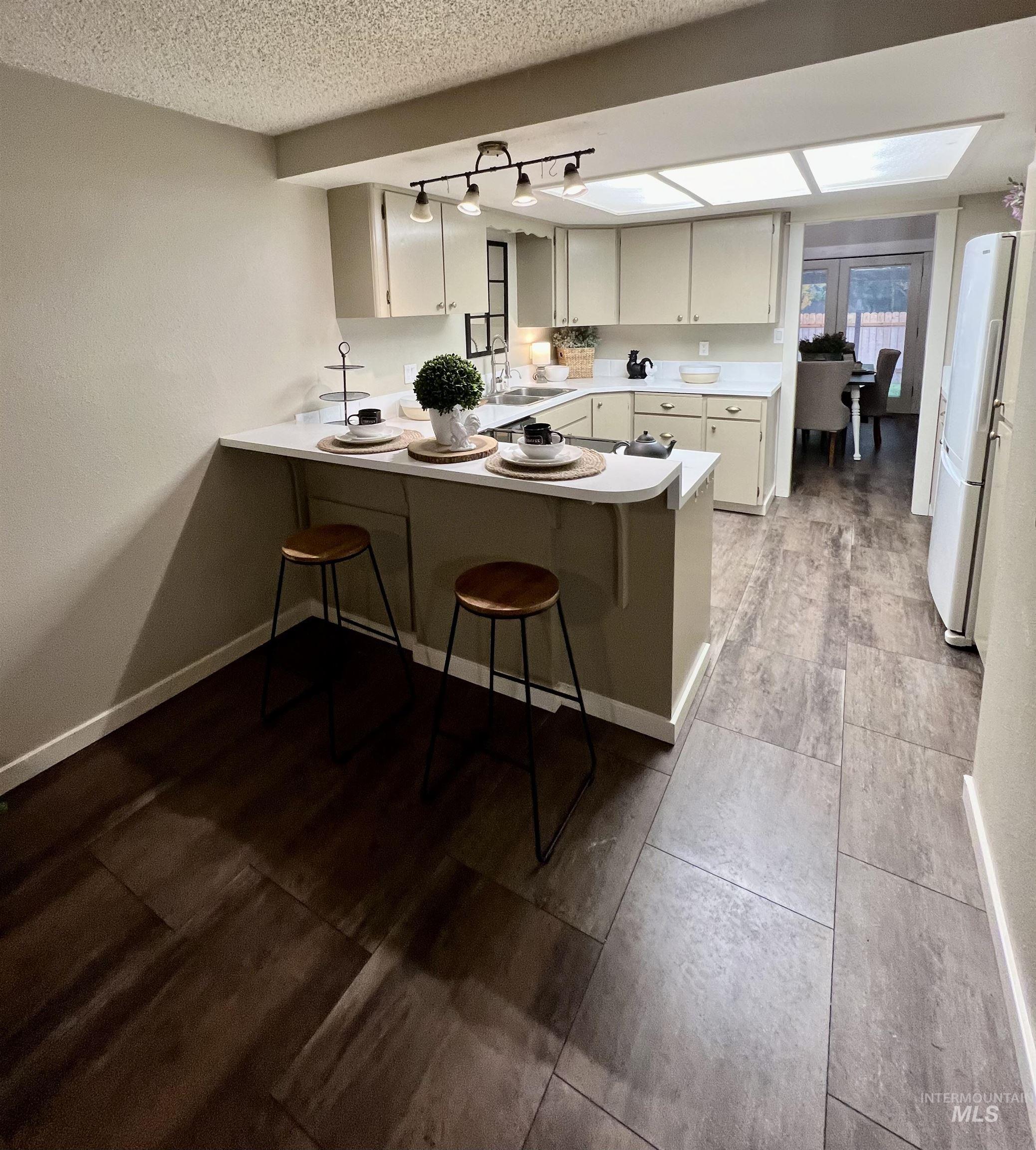 Kitchen featuring a kitchen breakfast bar, a peninsula, light countertops, freestanding refrigerator, and white cabinetry