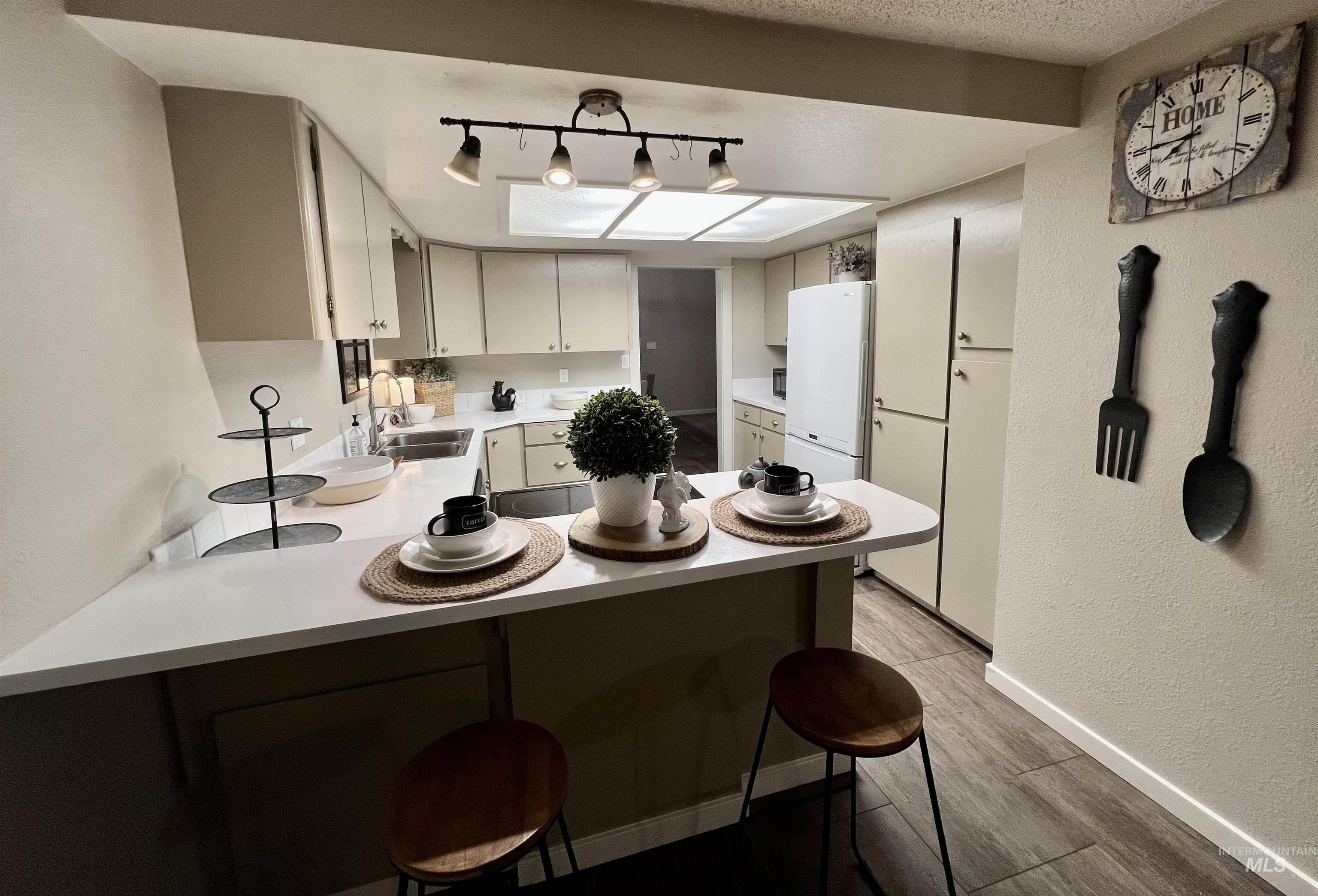 Kitchen featuring a kitchen bar, light countertops, a textured wall, dark wood-type flooring, and a peninsula