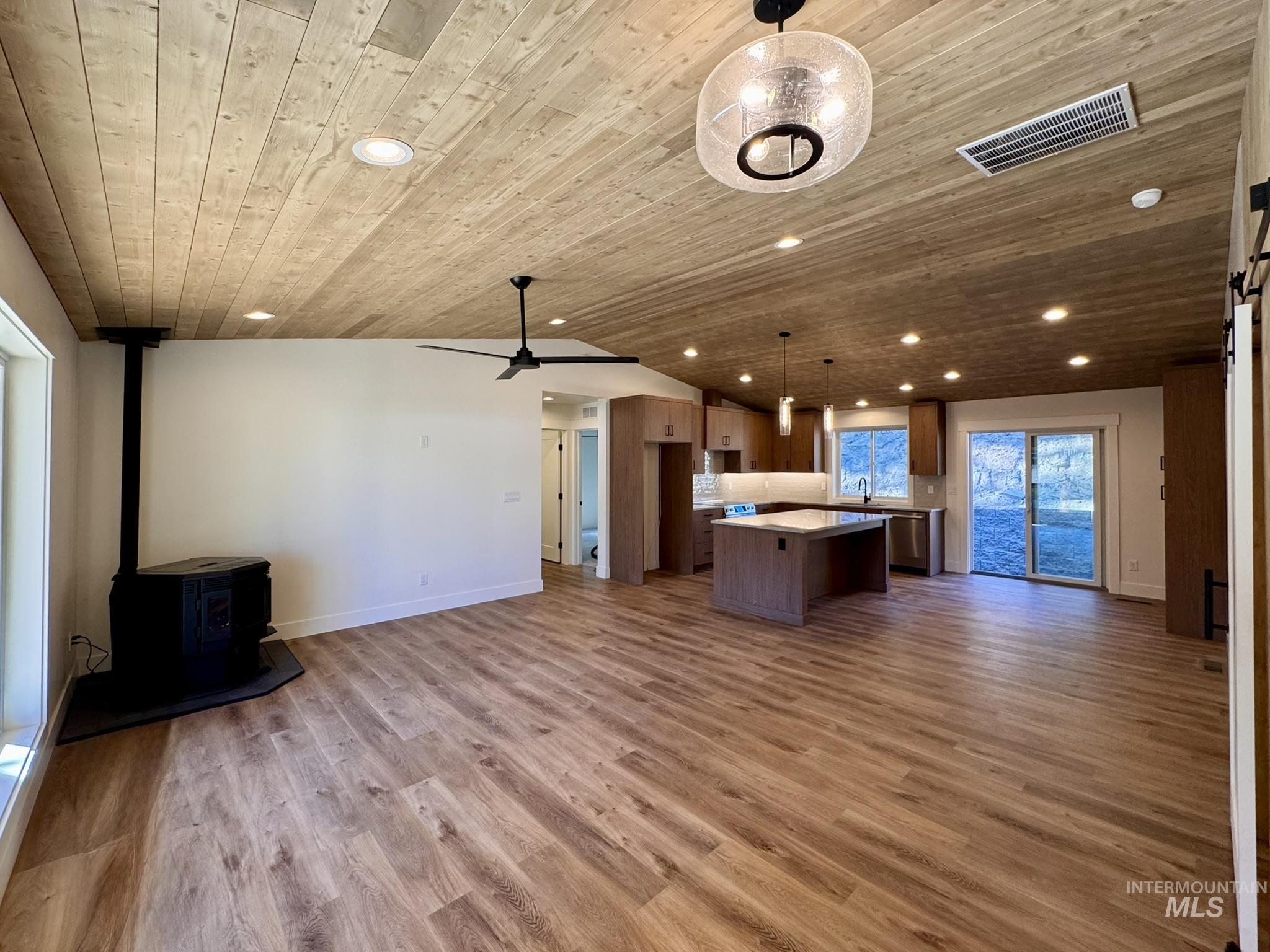 Kitchen featuring open floor plan, wood ceiling, hanging light fixtures, a kitchen island, and a wood stove