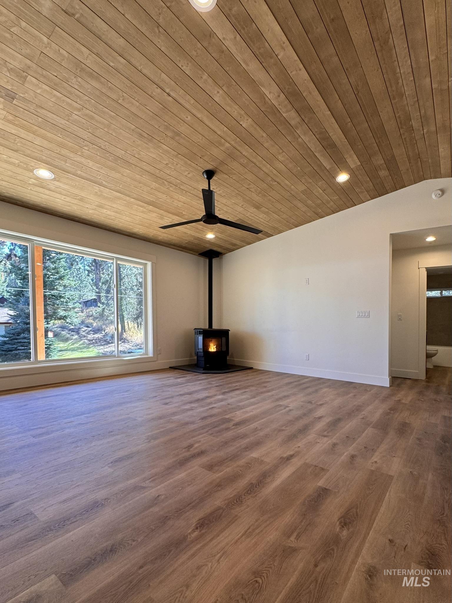 Unfurnished living room featuring a wood stove, recessed lighting, wood finished floors, and wooden ceiling