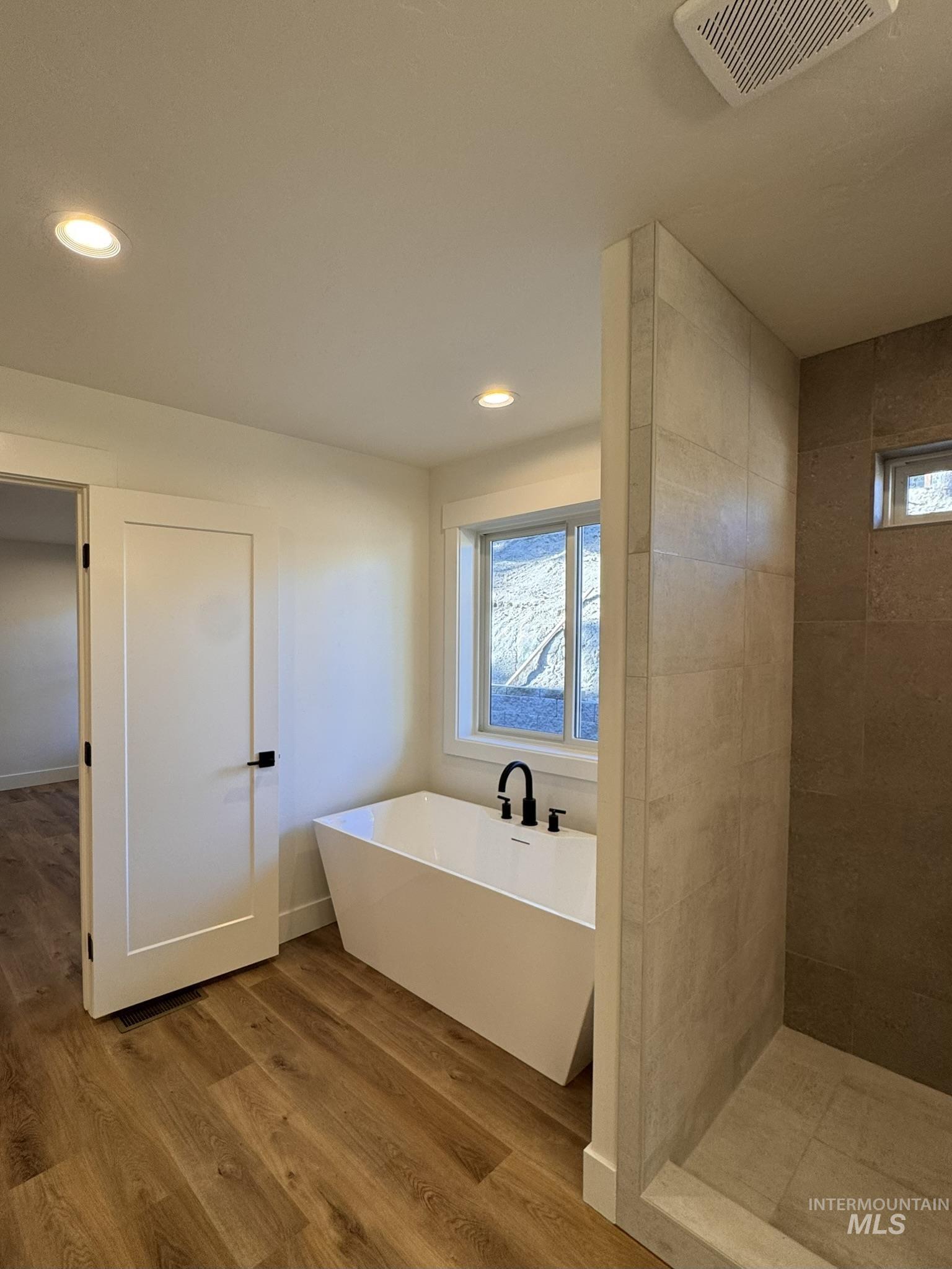 Full bath with a freestanding tub, plenty of natural light, recessed lighting, light wood-style flooring, and a stall shower