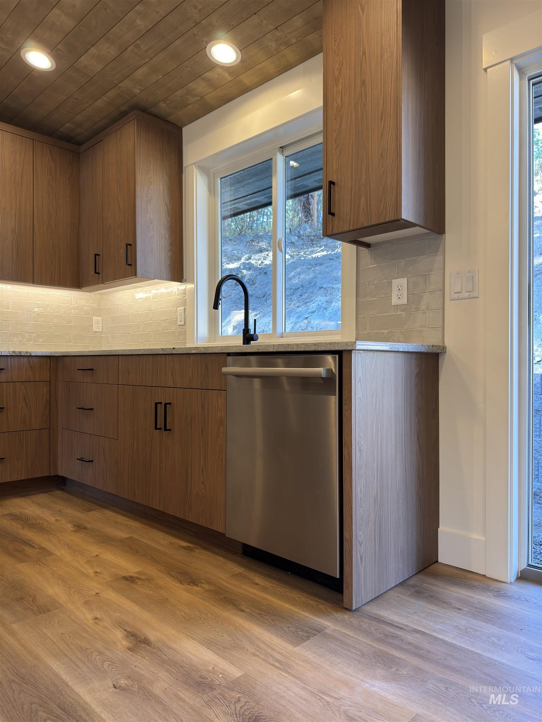 Kitchen with backsplash, dark wood-style floors, dishwasher, light stone counters, and recessed lighting