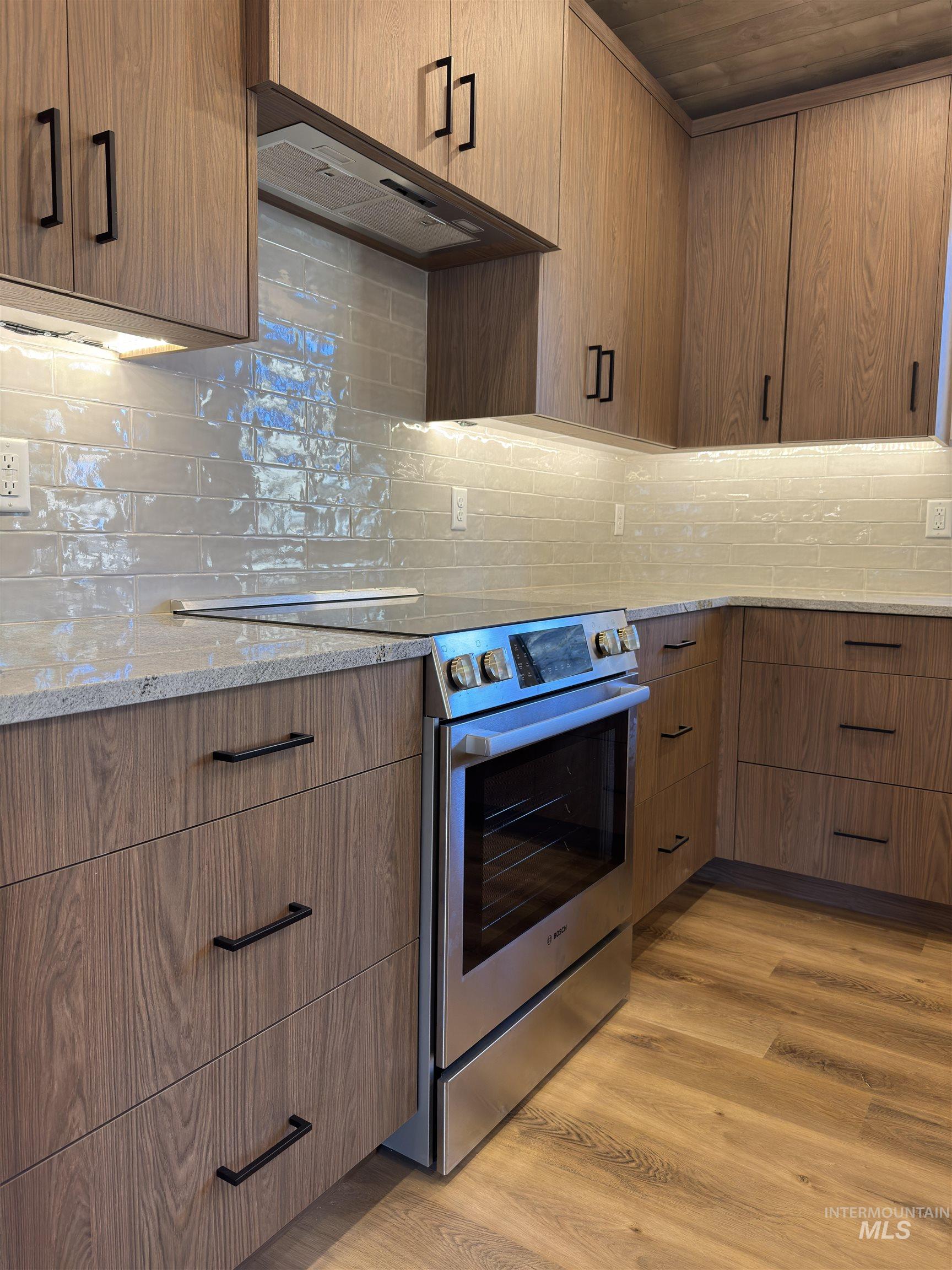 Kitchen featuring stainless steel range with electric cooktop, light wood-type flooring, light stone countertops, under cabinet range hood, and modern cabinets