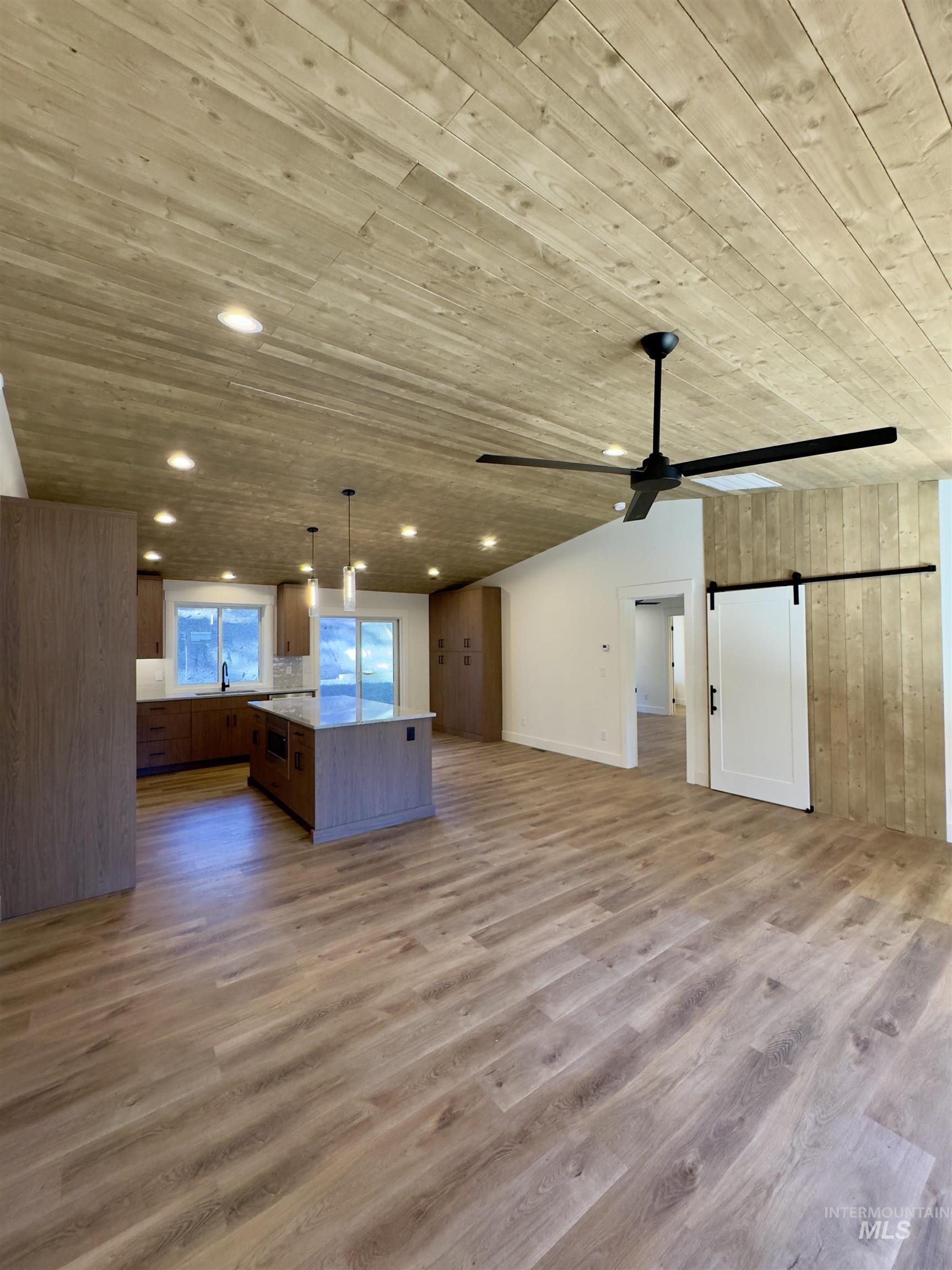 Unfurnished living room with wooden walls, light wood finished floors, a ceiling fan, a barn door, and recessed lighting