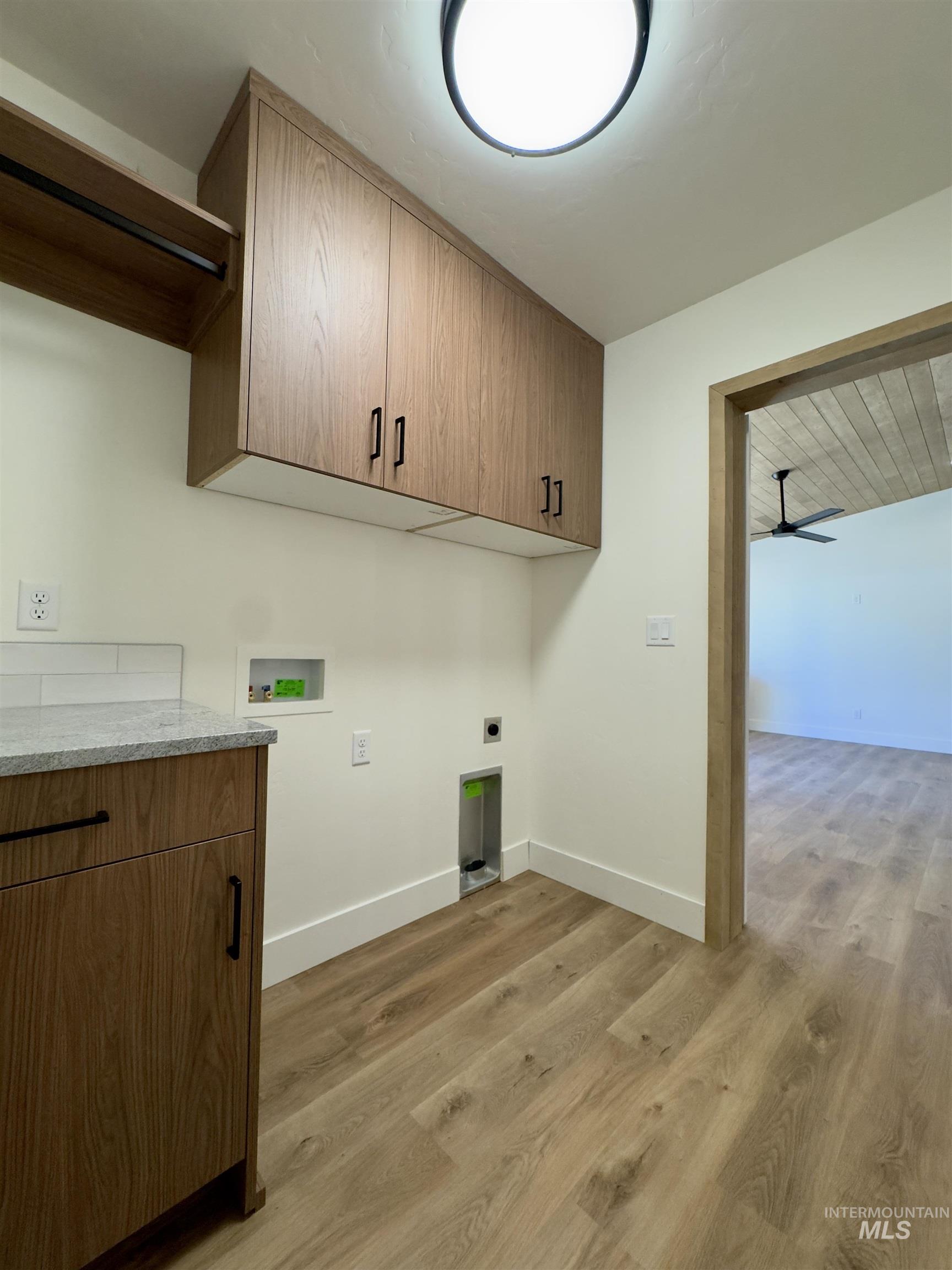 Washroom with light wood finished floors, hookup for a washing machine, ceiling fan, electric dryer hookup, and cabinet space