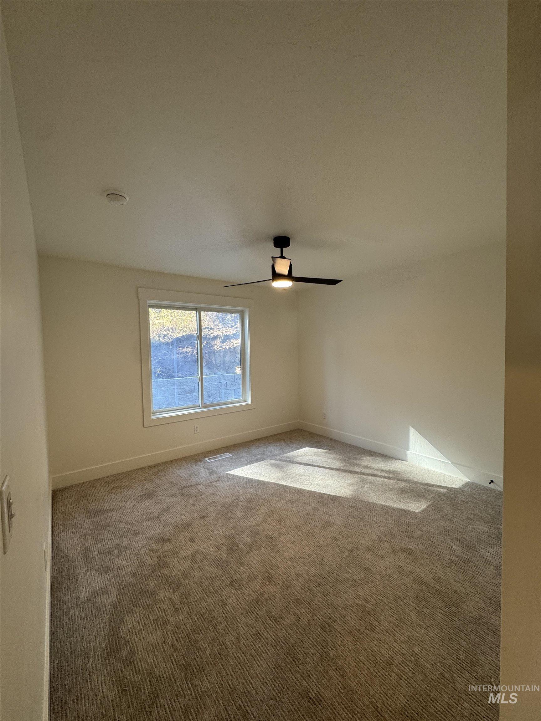 Carpeted spare room featuring ceiling fan and baseboards
