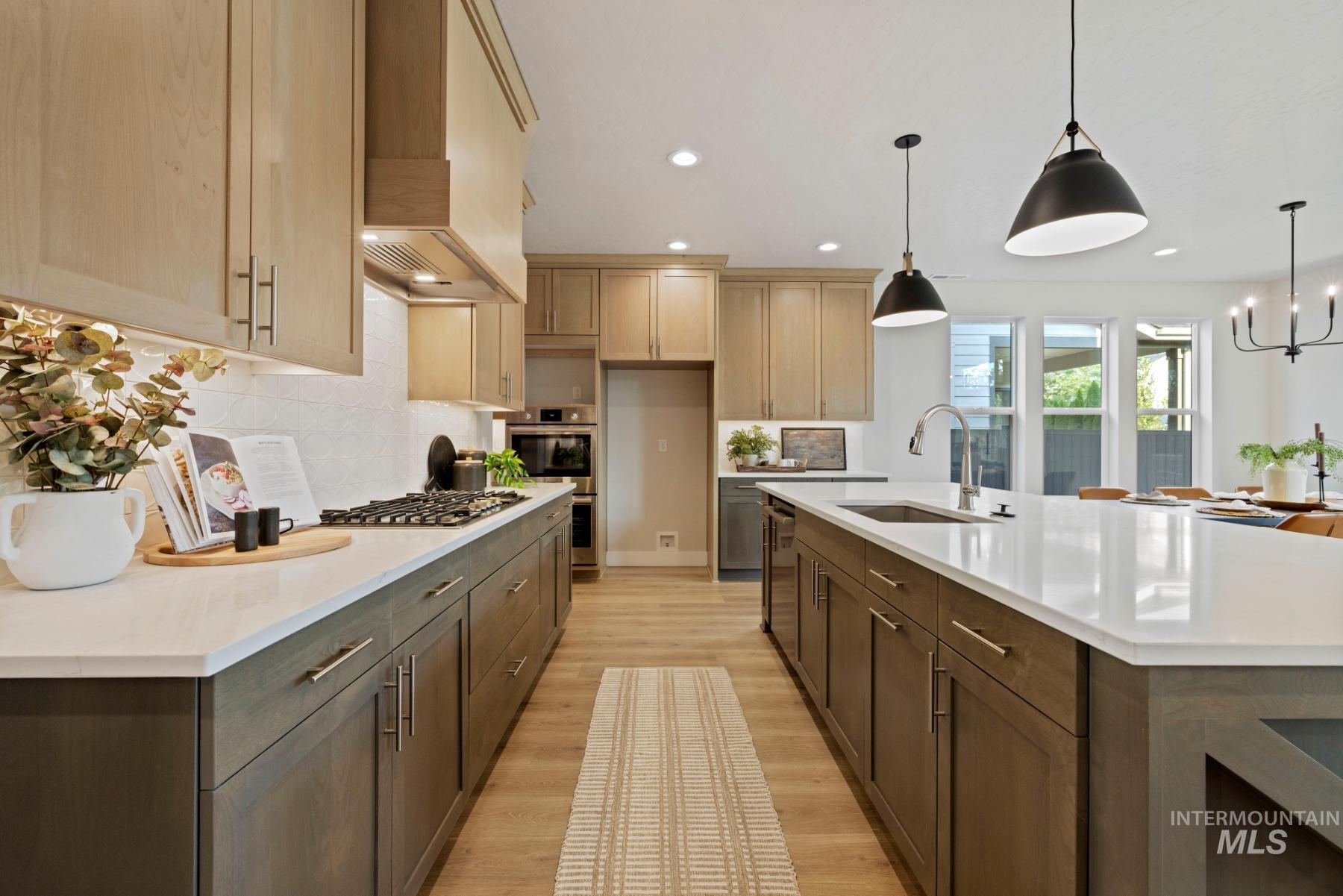 Kitchen with light wood-type flooring, hanging light fixtures, a chandelier, backsplash, and light stone counters