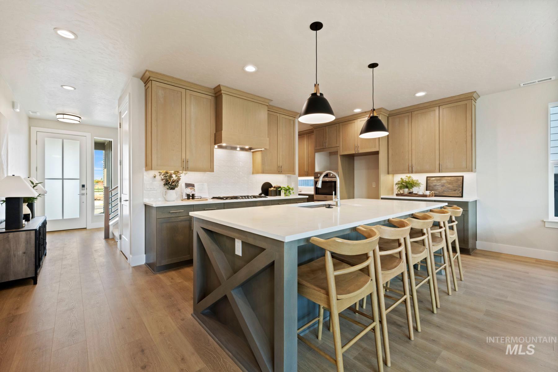 Kitchen with decorative backsplash, a kitchen breakfast bar, hanging light fixtures, an island with sink, and light wood-type flooring