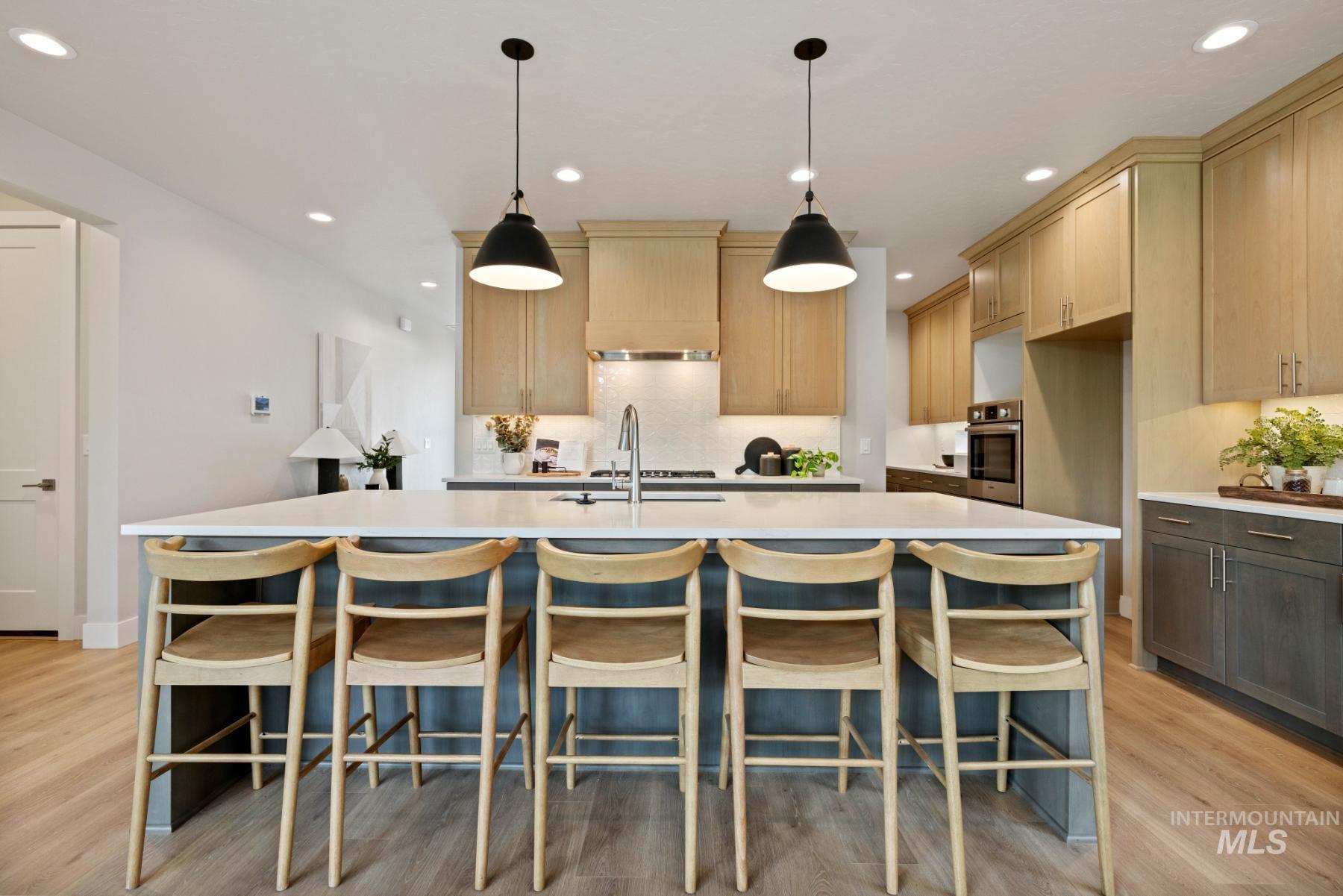 Kitchen with a center island with sink, pendant lighting, recessed lighting, light wood finished floors, and a breakfast bar