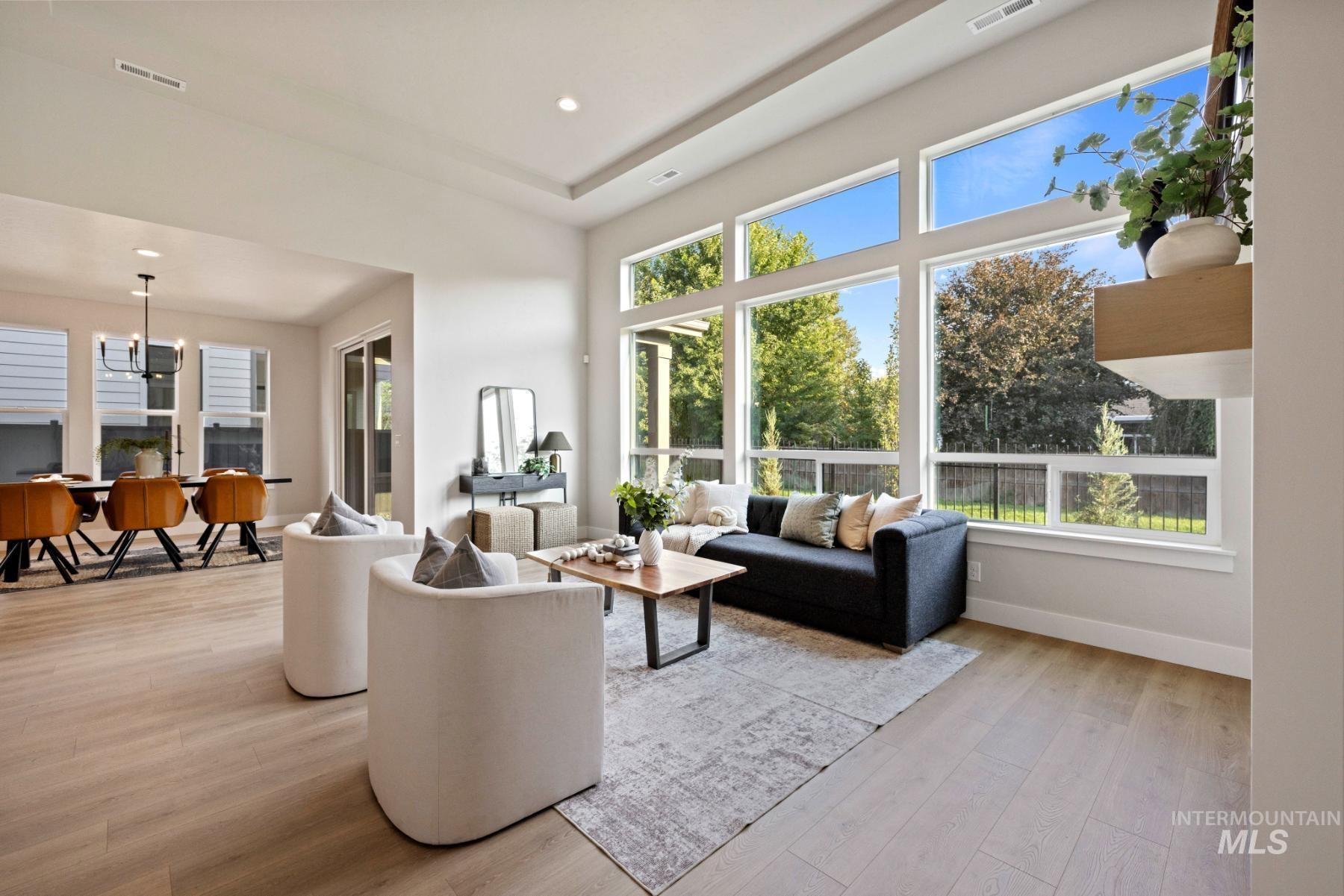 Living room featuring light wood-type flooring, a chandelier, recessed lighting, a raised ceiling, and a towering ceiling