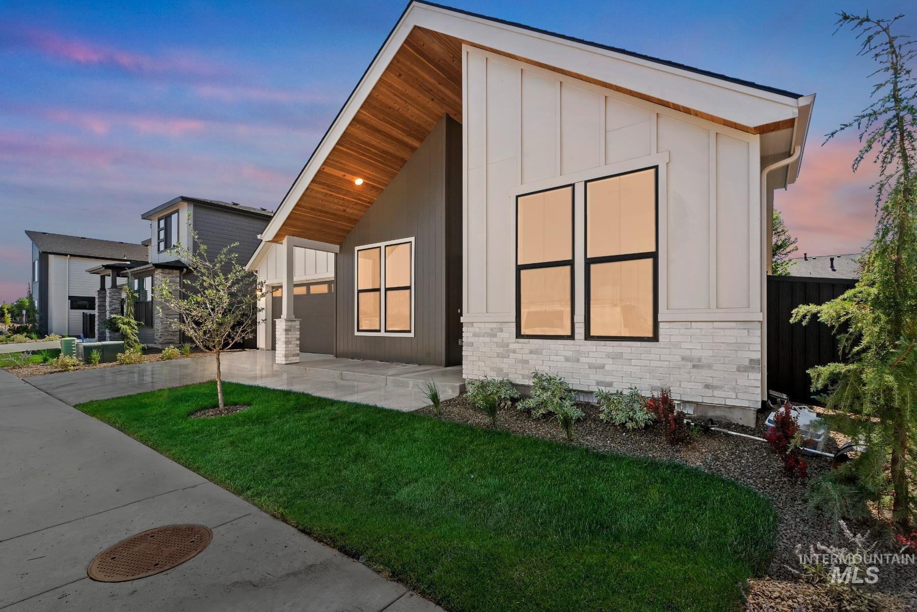 View of front facade featuring concrete driveway, board and batten siding, a front yard, a patio, and an attached garage