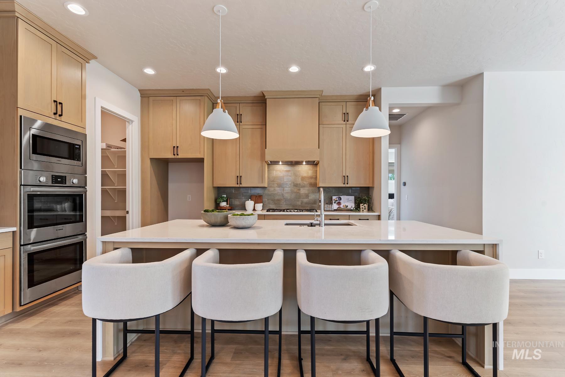 Kitchen with light wood-type flooring, decorative light fixtures, stainless steel appliances, light stone counters, and tasteful backsplash