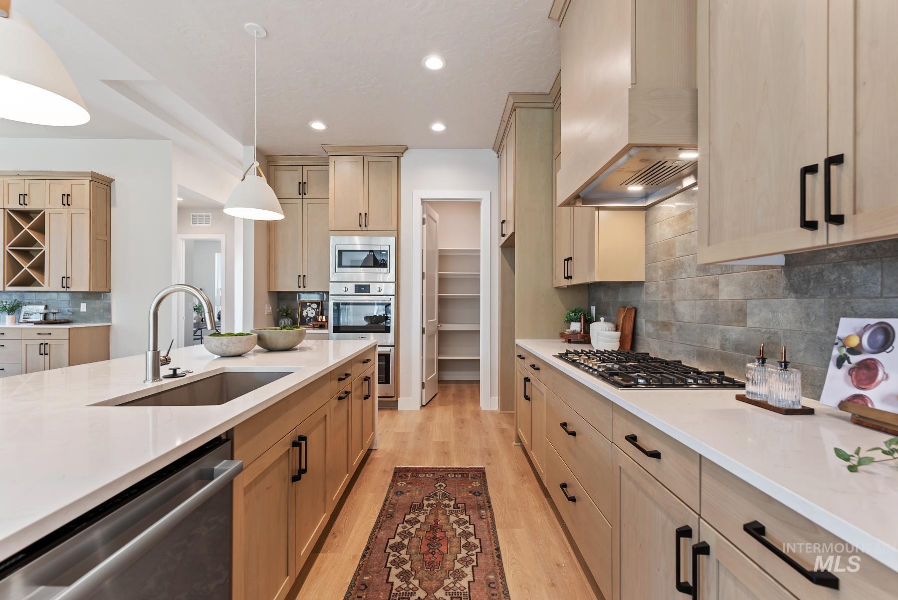 Kitchen featuring decorative backsplash, light wood finished floors, appliances with stainless steel finishes, light stone countertops, and hanging light fixtures