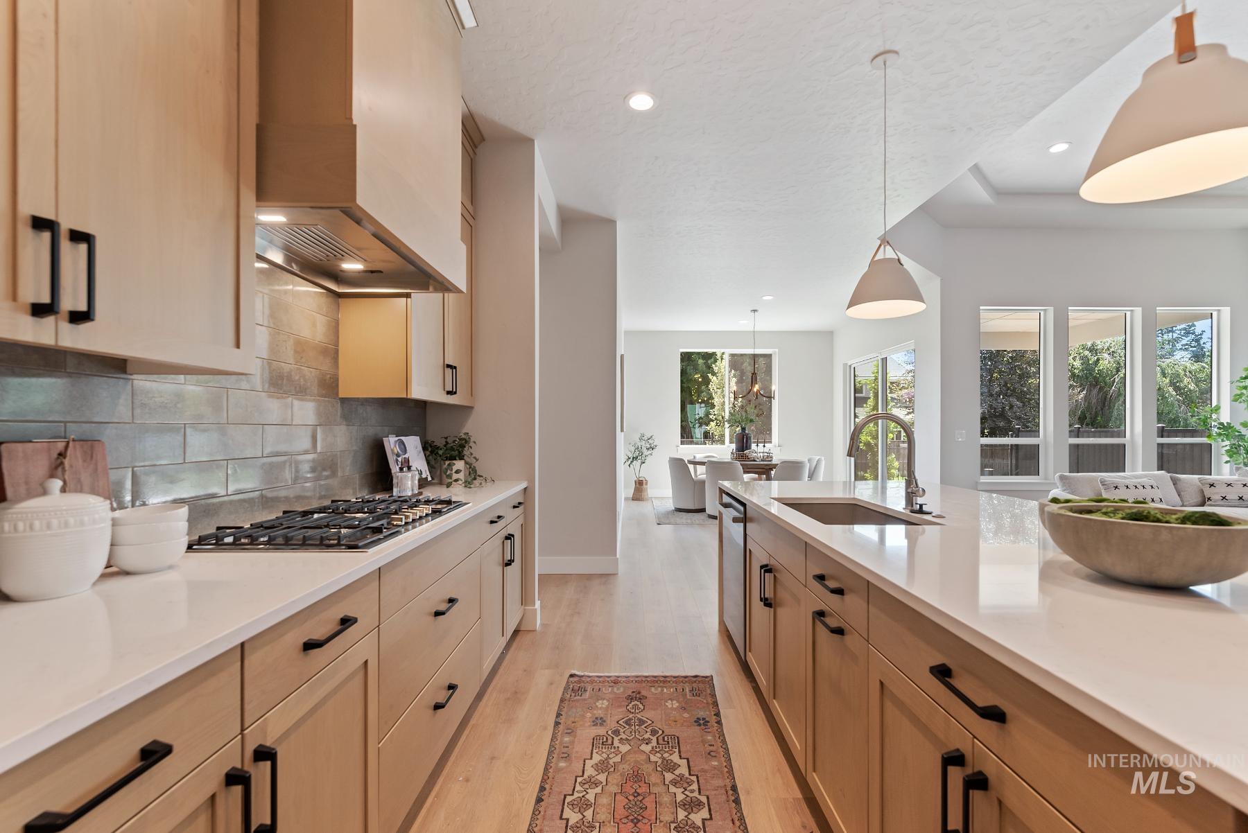 Kitchen with light wood-type flooring, pendant lighting, wall chimney range hood, light brown cabinets, and tasteful backsplash