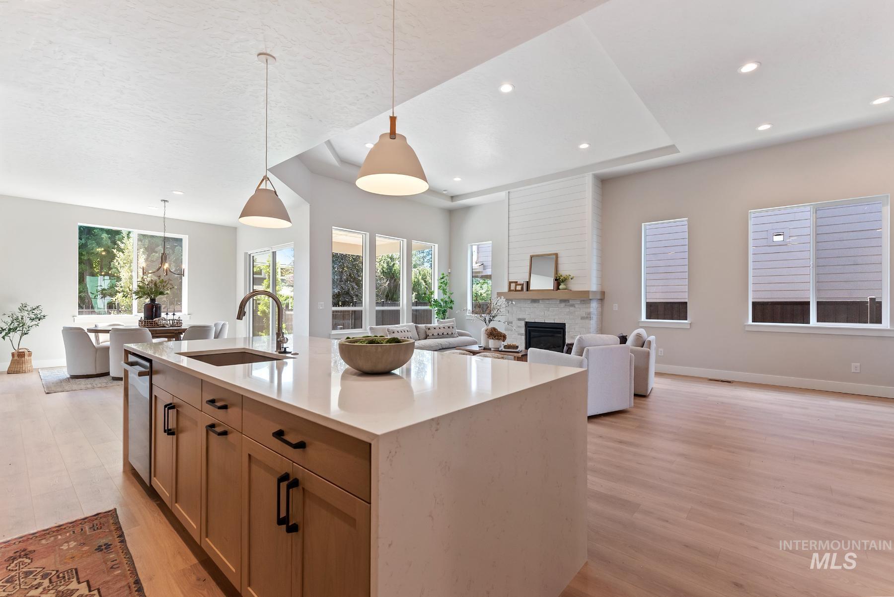 Kitchen featuring a fireplace, pendant lighting, open floor plan, light wood finished floors, and light stone countertops