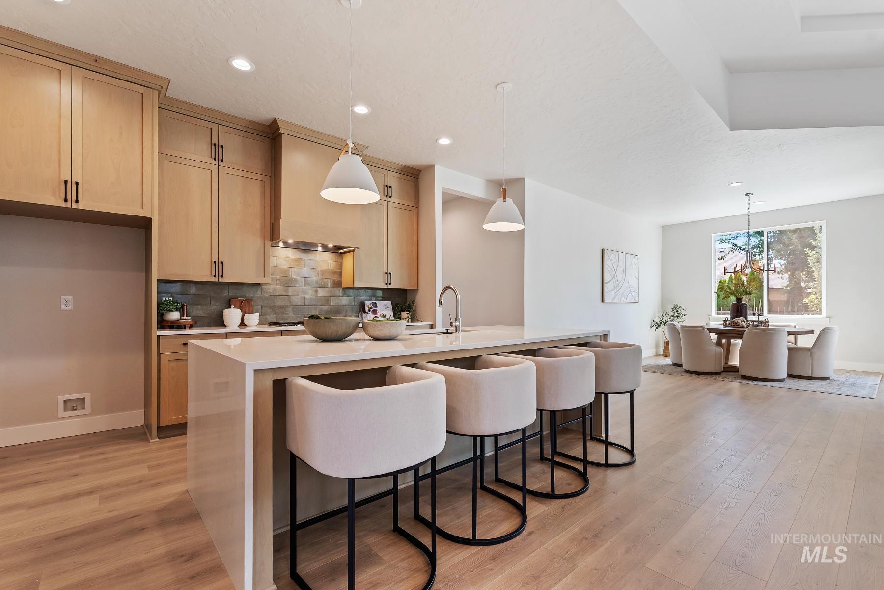 Kitchen with hanging light fixtures, light stone counters, a breakfast bar, light wood-type flooring, and recessed lighting