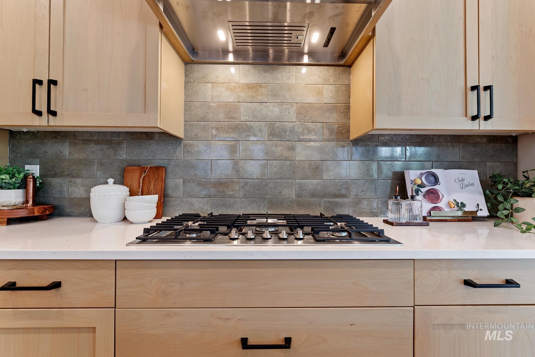 Kitchen featuring light brown cabinetry, tasteful backsplash, exhaust hood, and light stone countertops