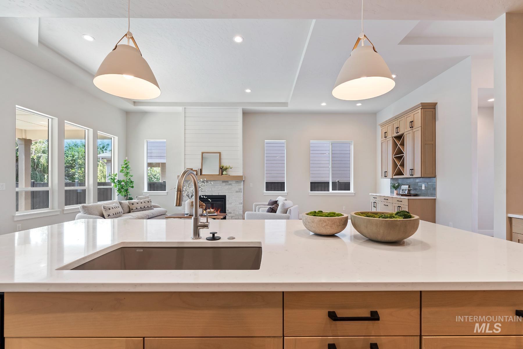 Kitchen with hanging light fixtures, a warm lit fireplace, light stone counters, open floor plan, and recessed lighting