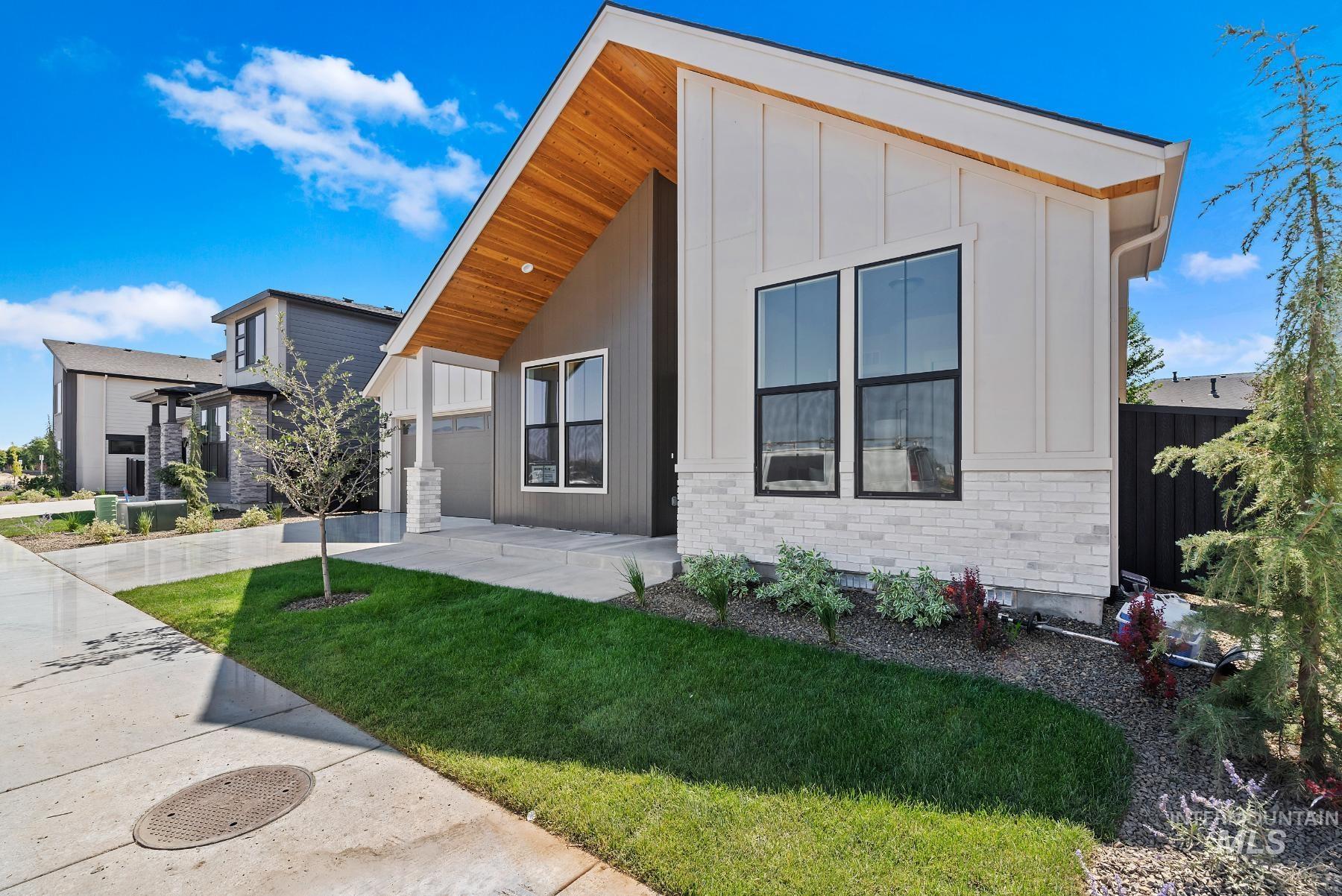 View of front facade with a garage, driveway, a front lawn, stone siding, and board and batten siding