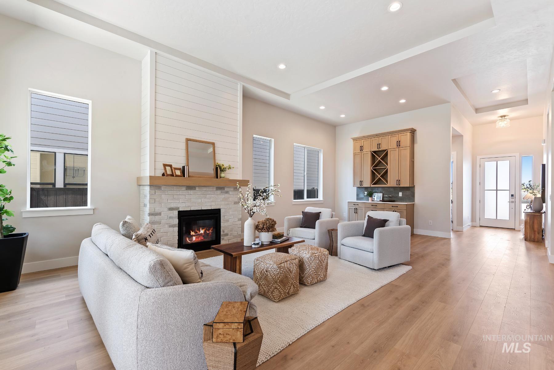 Living room featuring a dry bar, light wood-type flooring, a fireplace, recessed lighting, and a tray ceiling