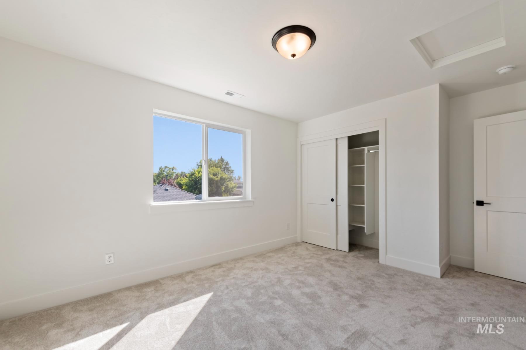 Unfurnished bedroom featuring attic access, carpet flooring, and a closet