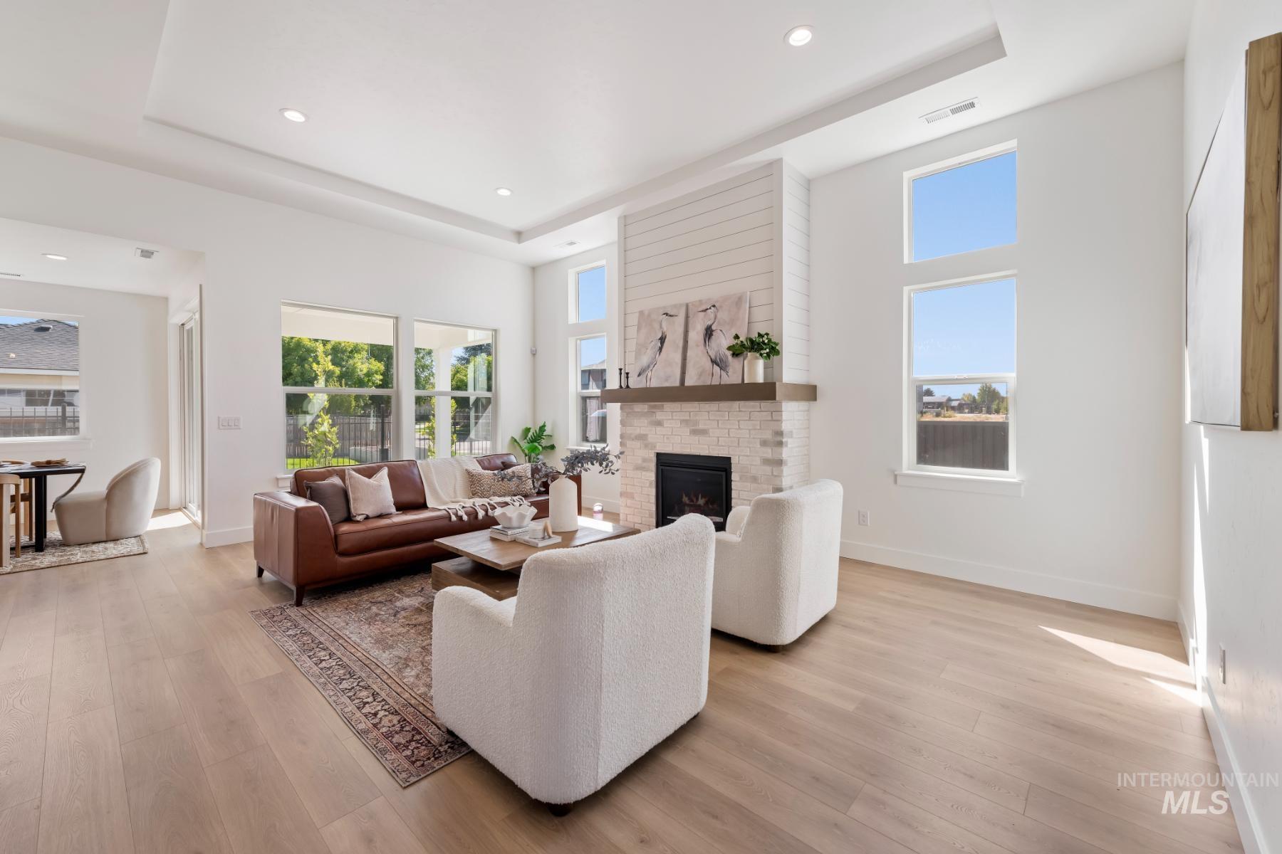 Living room featuring a tray ceiling, a brick fireplace, healthy amount of natural light, recessed lighting, and a towering ceiling