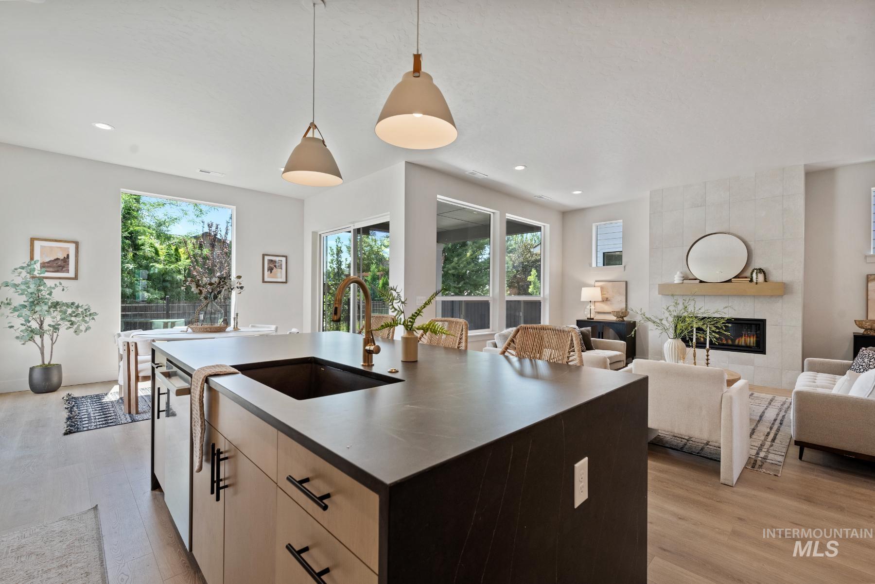 Kitchen with decorative light fixtures, a kitchen island with sink, light wood finished floors, a fireplace, and light brown cabinets