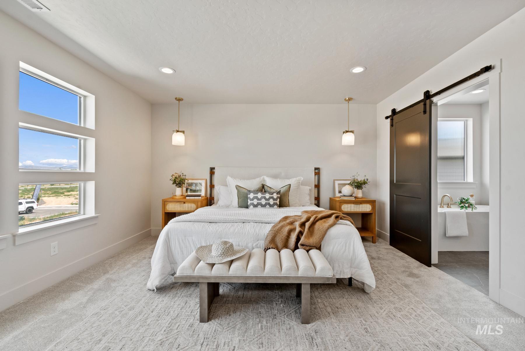 Carpeted bedroom featuring a barn door, multiple windows, ensuite bathroom, and recessed lighting