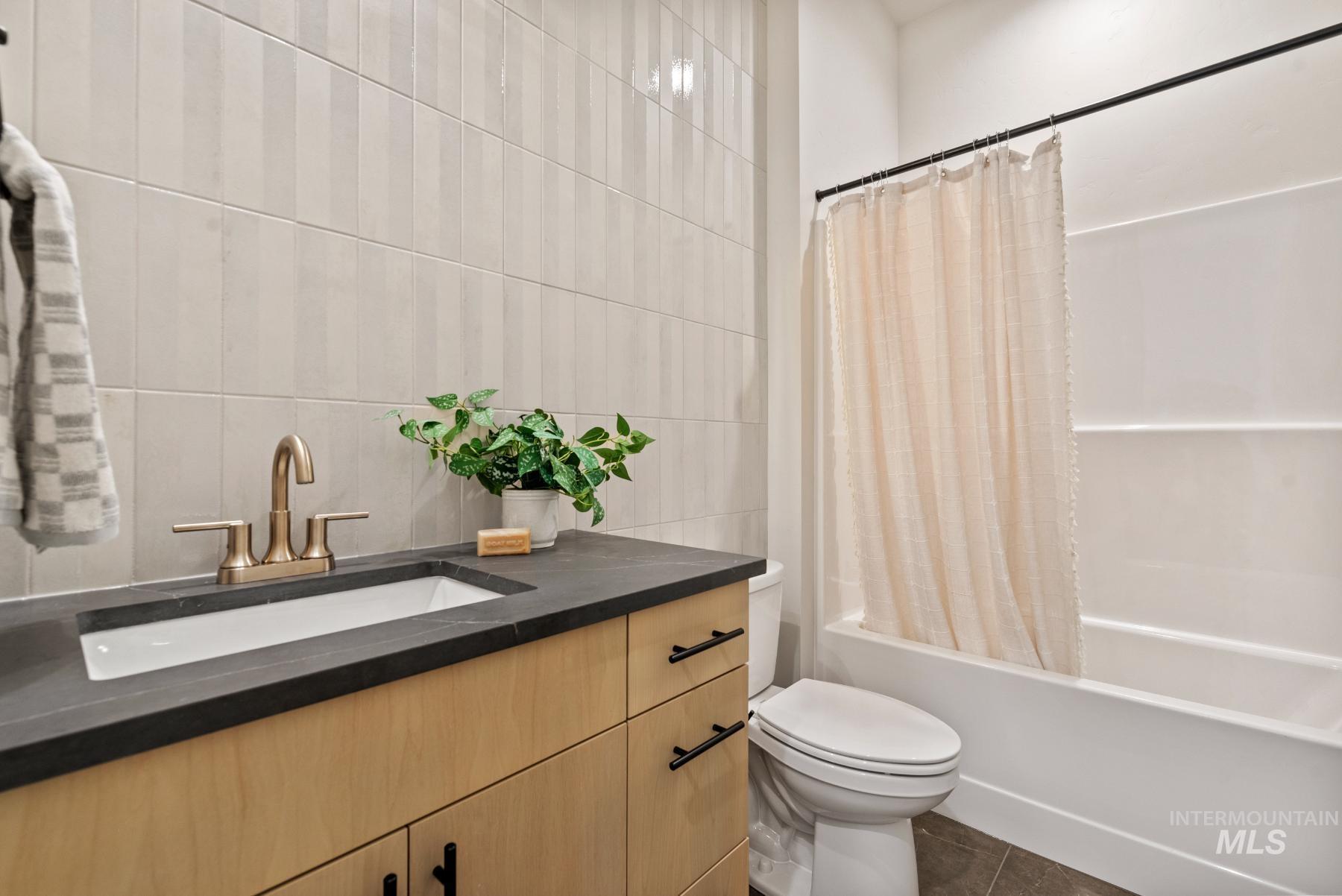 Bathroom with vanity, shower / tub combo with curtain, tile walls, and dark tile patterned flooring