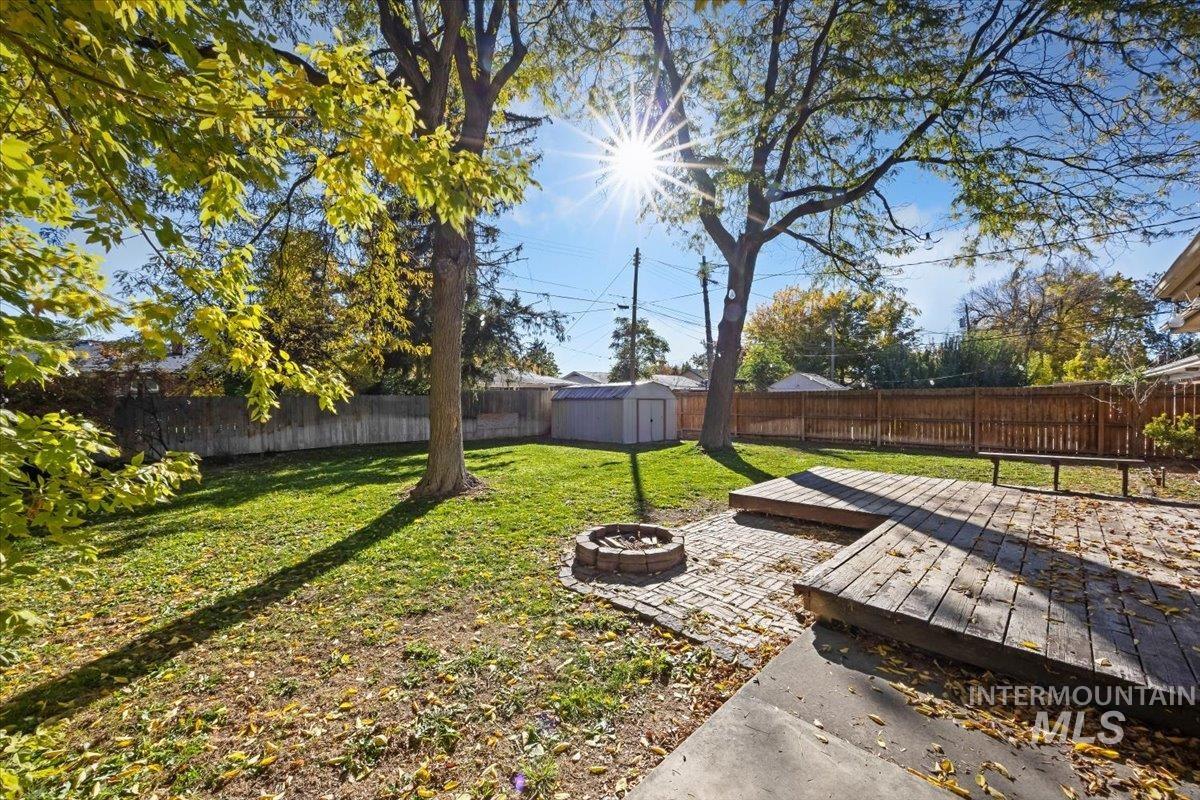 Fenced backyard featuring an outdoor fire pit, a wooden deck, and a storage unit
