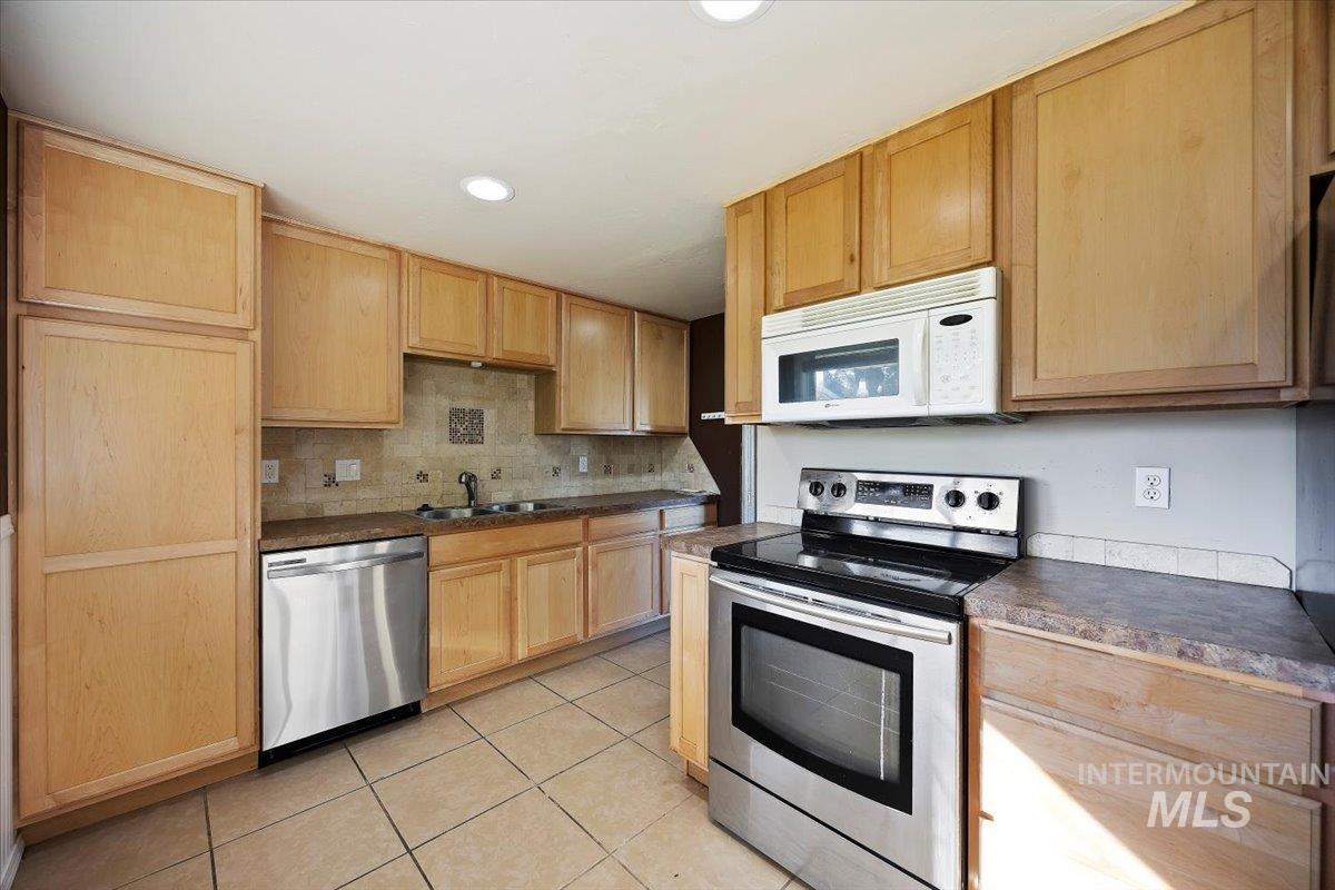 Kitchen featuring stainless steel appliances, light brown cabinetry, light tile patterned floors, tasteful backsplash, and recessed lighting