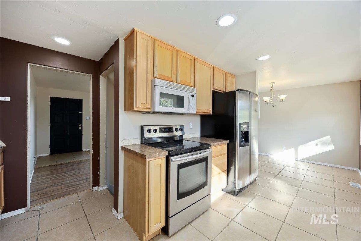 Kitchen with light brown cabinetry, electric range, light tile patterned flooring, white microwave, and recessed lighting