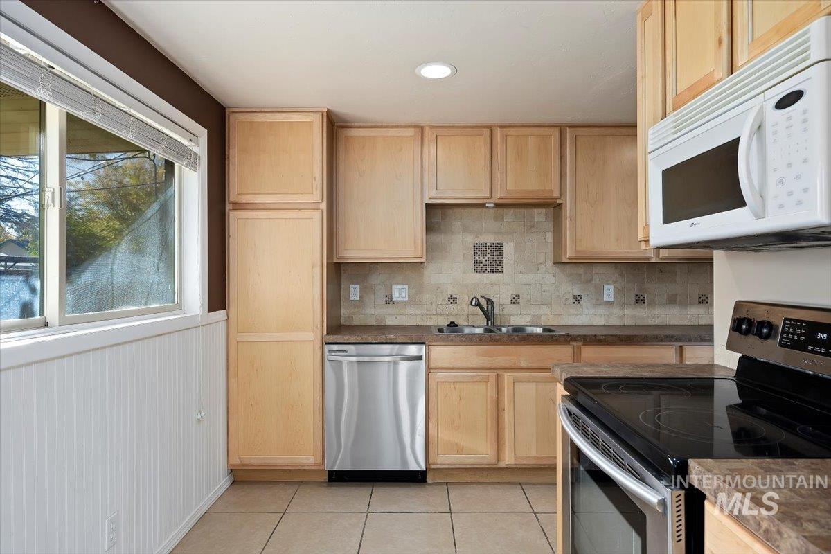 Kitchen with stainless steel appliances, light brown cabinetry, backsplash, dark countertops, and light tile patterned floors