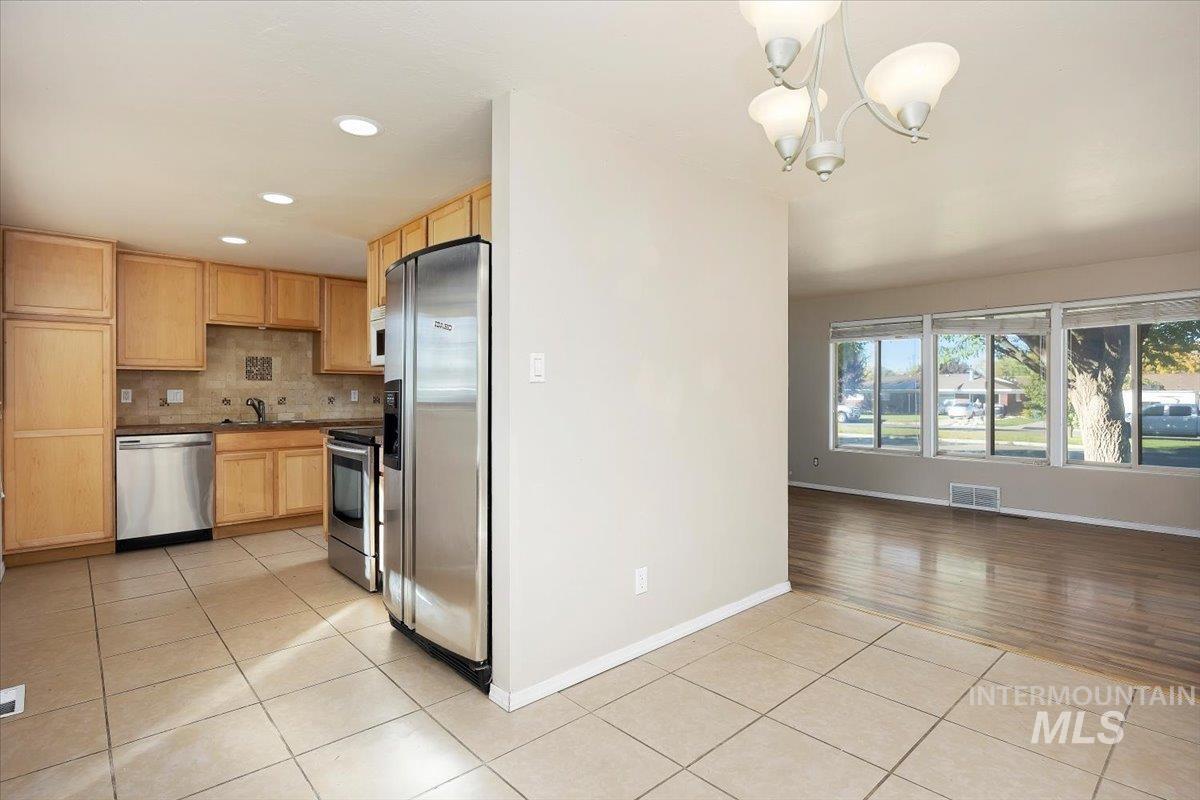 Kitchen with stainless steel appliances, backsplash, light tile patterned floors, dark countertops, and recessed lighting