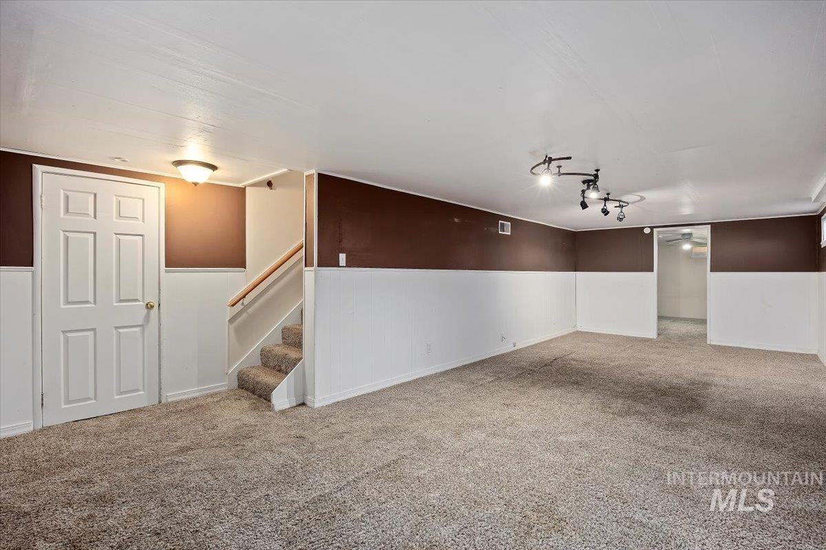 Finished basement with carpet flooring, a wainscoted wall, and stairway