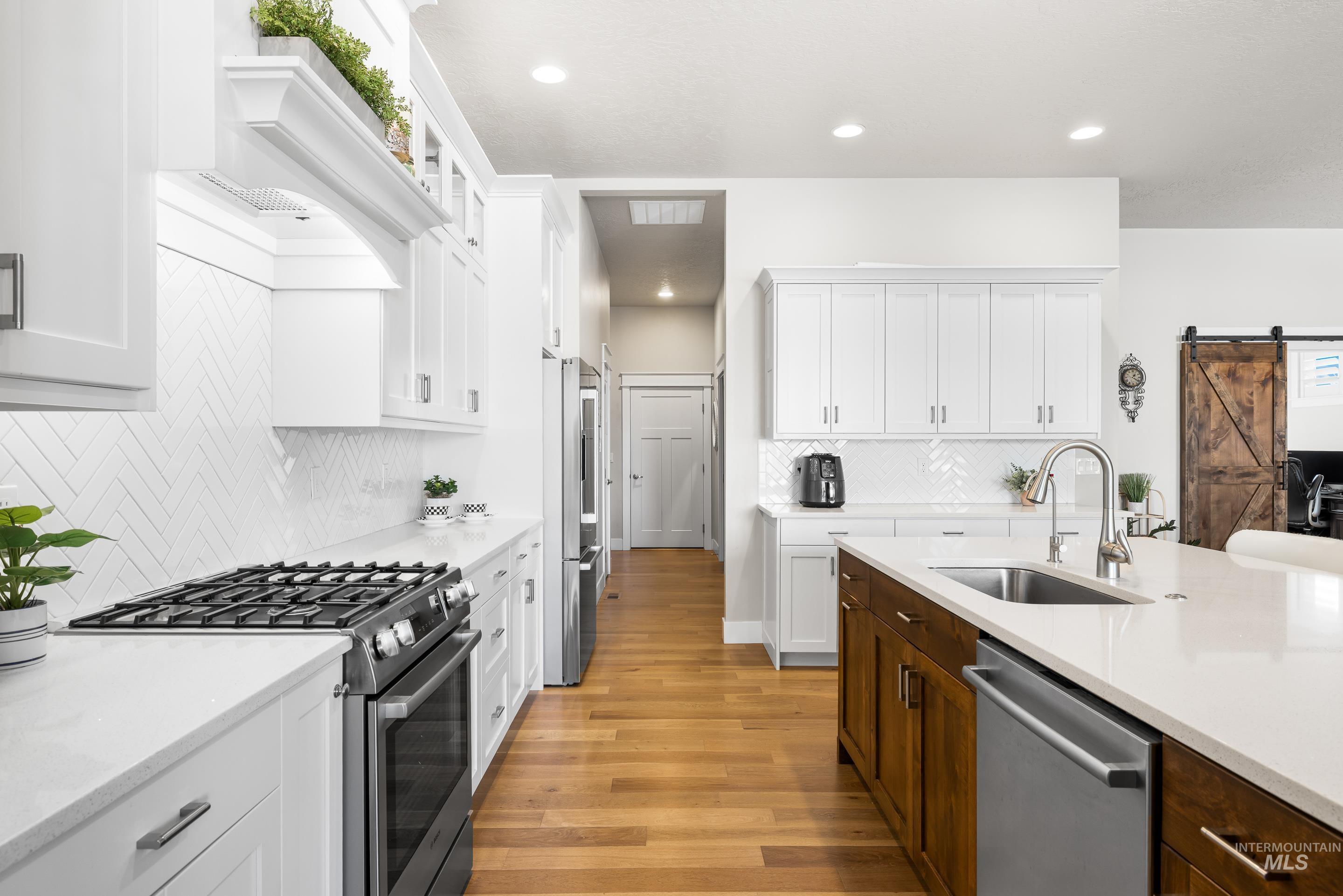 Kitchen with stainless steel appliances, a barn door, light wood-style floors, white cabinetry, and decorative backsplash